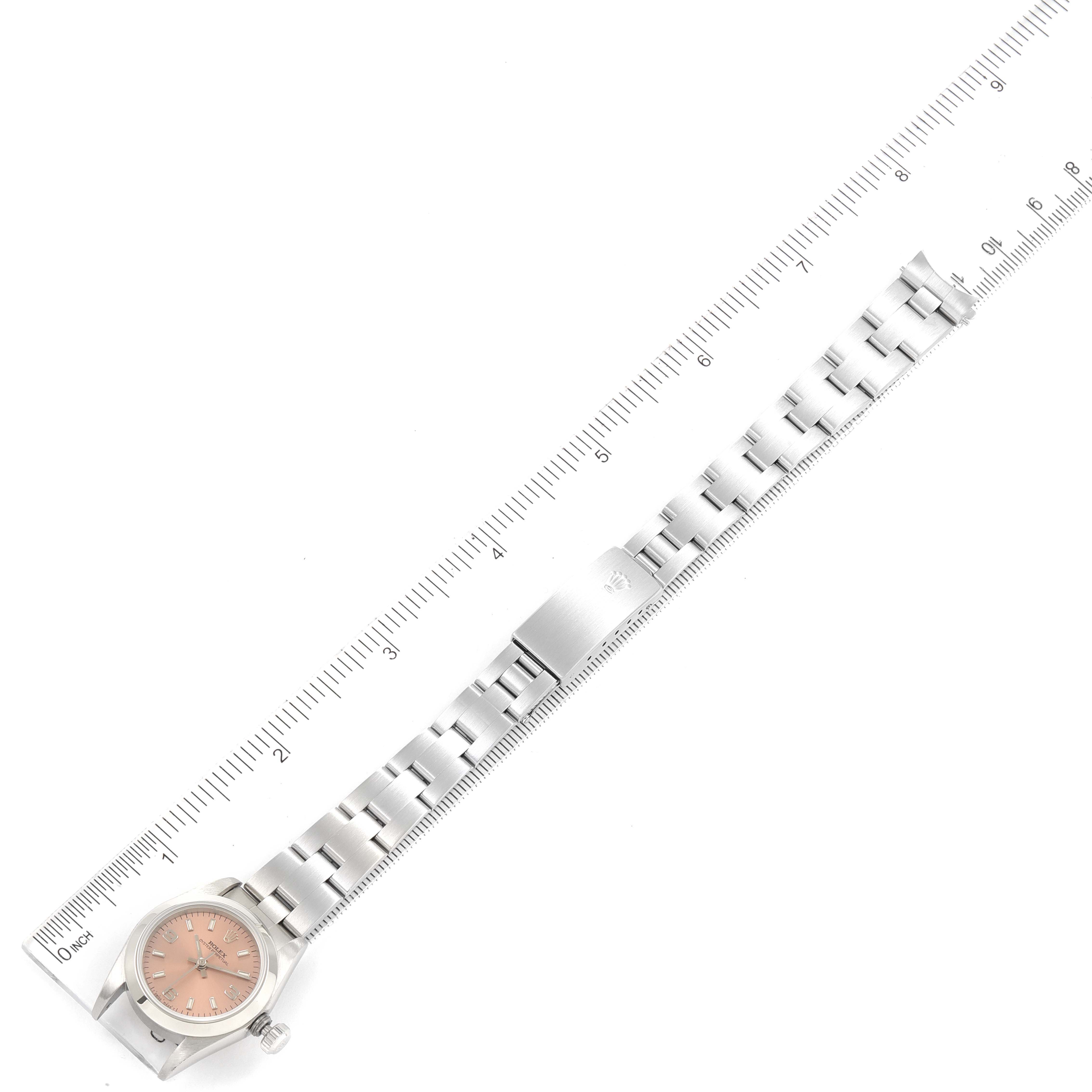 The image shows a top-down view of a Rolex Oyster Perpetual 67180 Women
s Stainless Steel Pink Dial 67180 Women
s Stainless Steel Pink Dial watch and its bracelet, placed alongside a ruler.