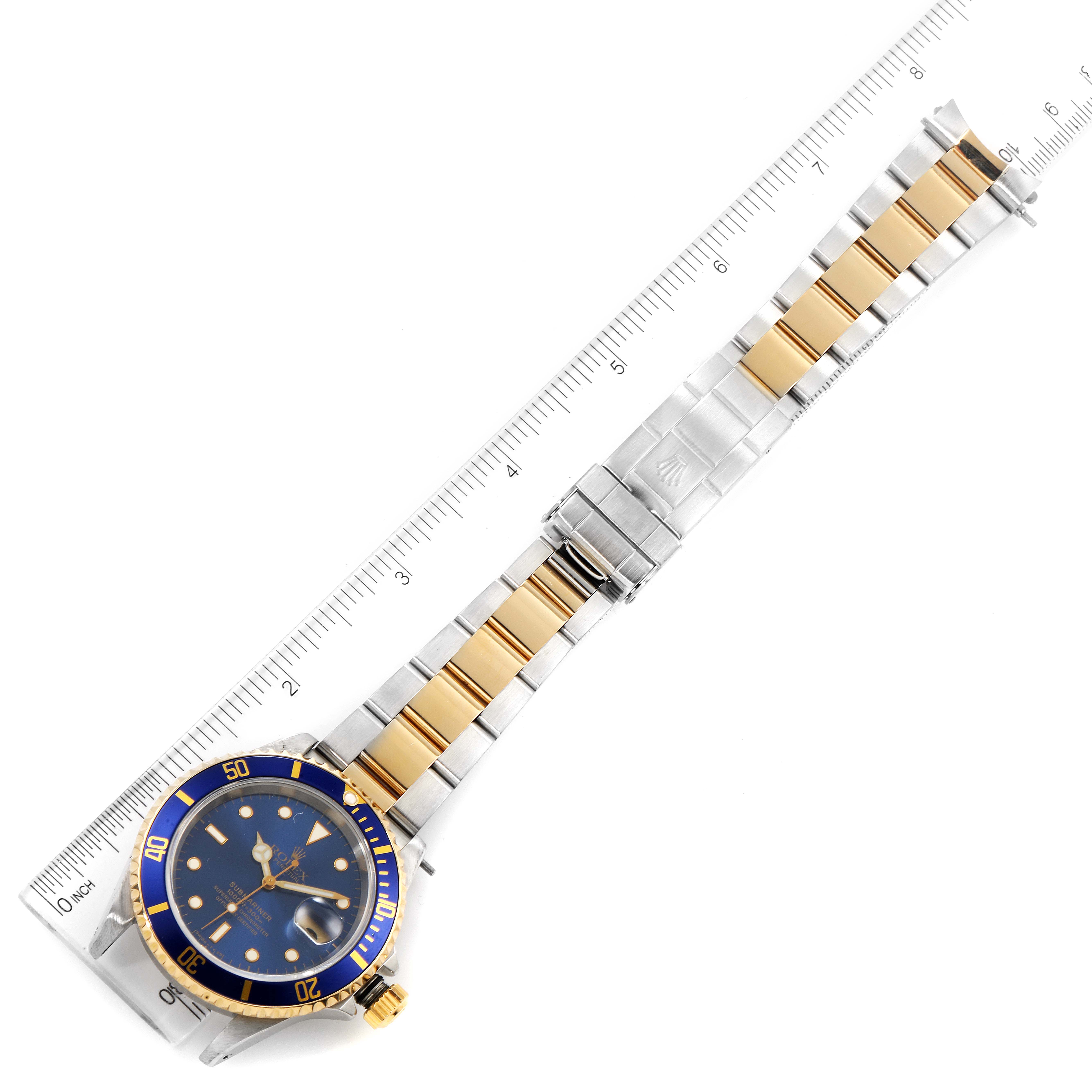 This image shows a Rolex Submariner 16613 Men
s Steel and Gold (two tone) Blue Dial 16613 Men
s Steel and Gold (two tone) Blue Dial watch with a blue dial, a gold and silver bracelet, and a measuring ruler for size reference.