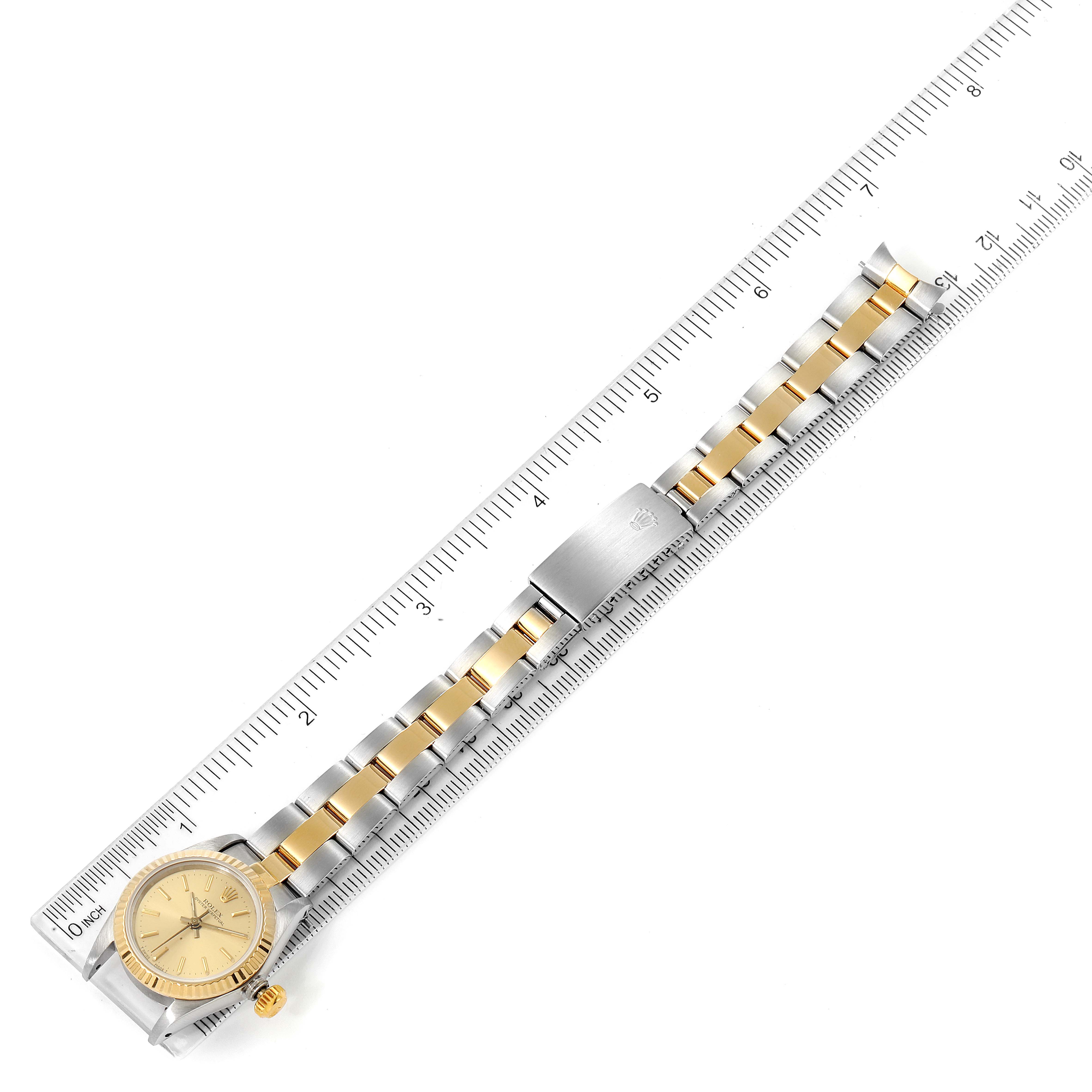 The image shows a top view of a Rolex Oyster Perpetual 67193 Women
s Steel and Gold (two tone) Champagne Dial 67193 Women
s Steel and Gold (two tone) Champagne Dial watch with a two-tone bracelet, displayed alongside a ruler.
