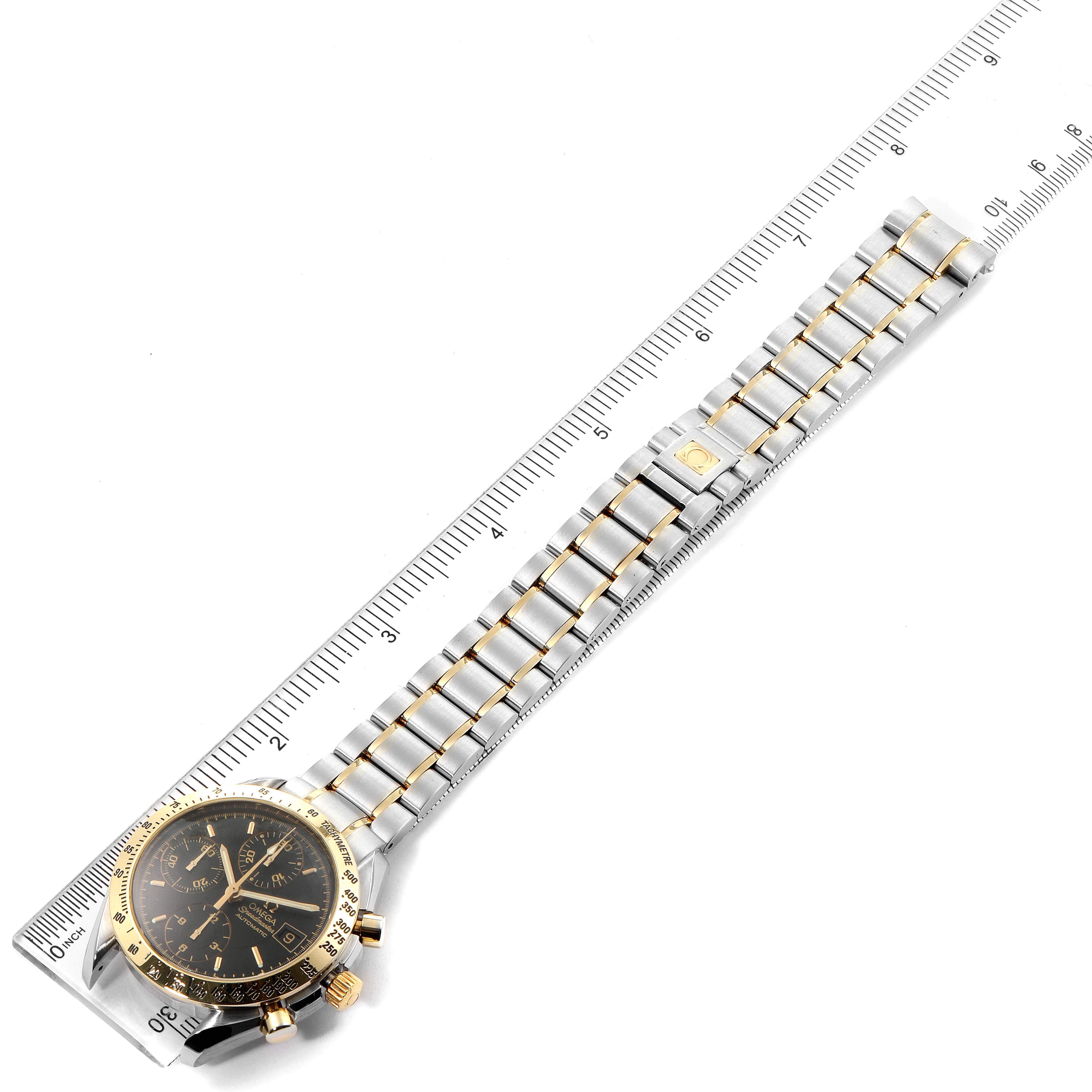 The Omega Speedmaster 3313.50.00 Men's Steel and Gold (two tone) Black Dial 3313.50.00 Men's Steel and Gold (two tone) Black Dial watch is shown at a diagonal angle, featuring its face, bezel, and full bracelet alongside a ruler.