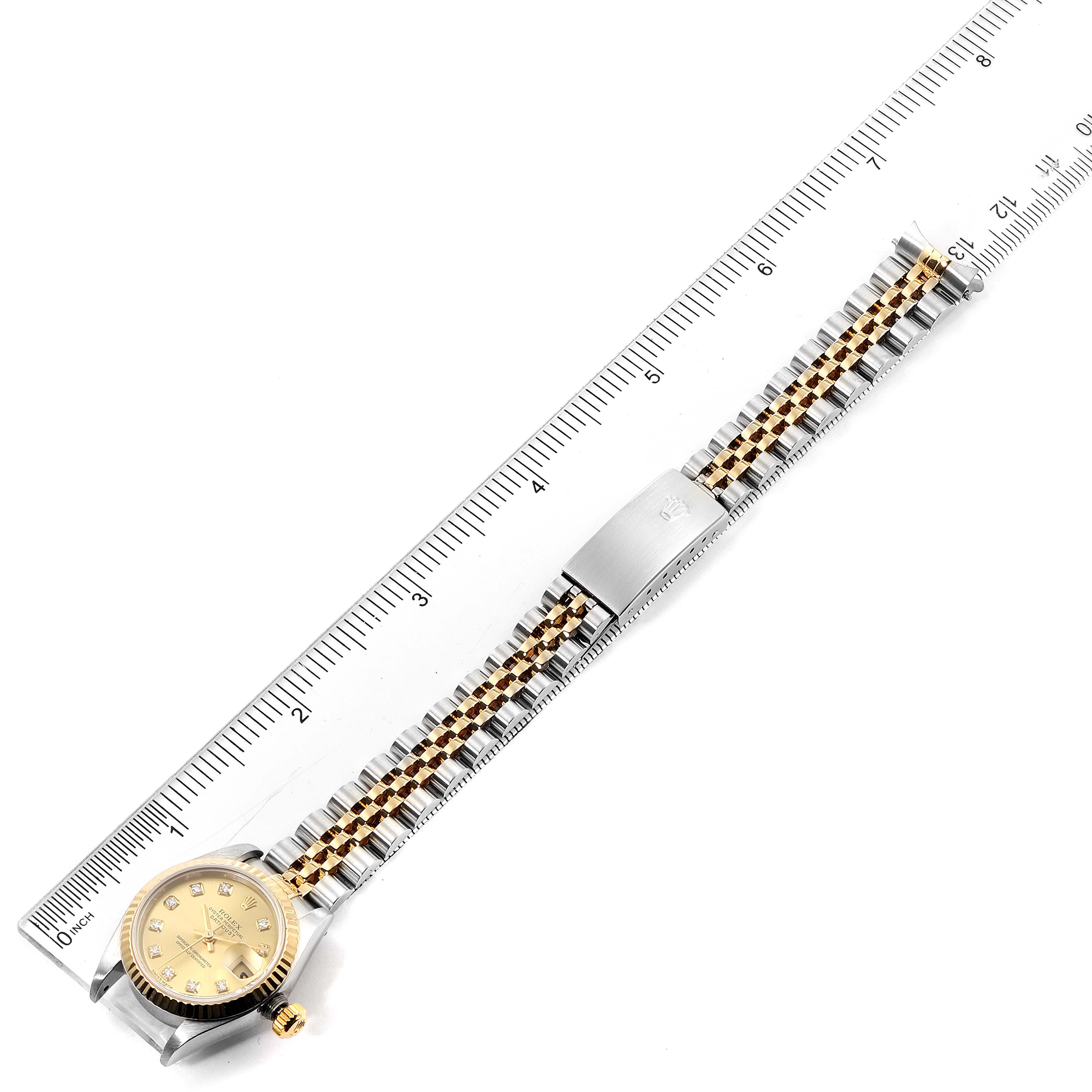 The image shows a top-down view of a Rolex Datejust 79173 Women
s Steel and Gold (two tone) Champagne Dial 79173 Women
s Steel and Gold (two tone) Champagne Dial watch, displaying its face, bracelet, and clasp, alongside a ruler for scale.