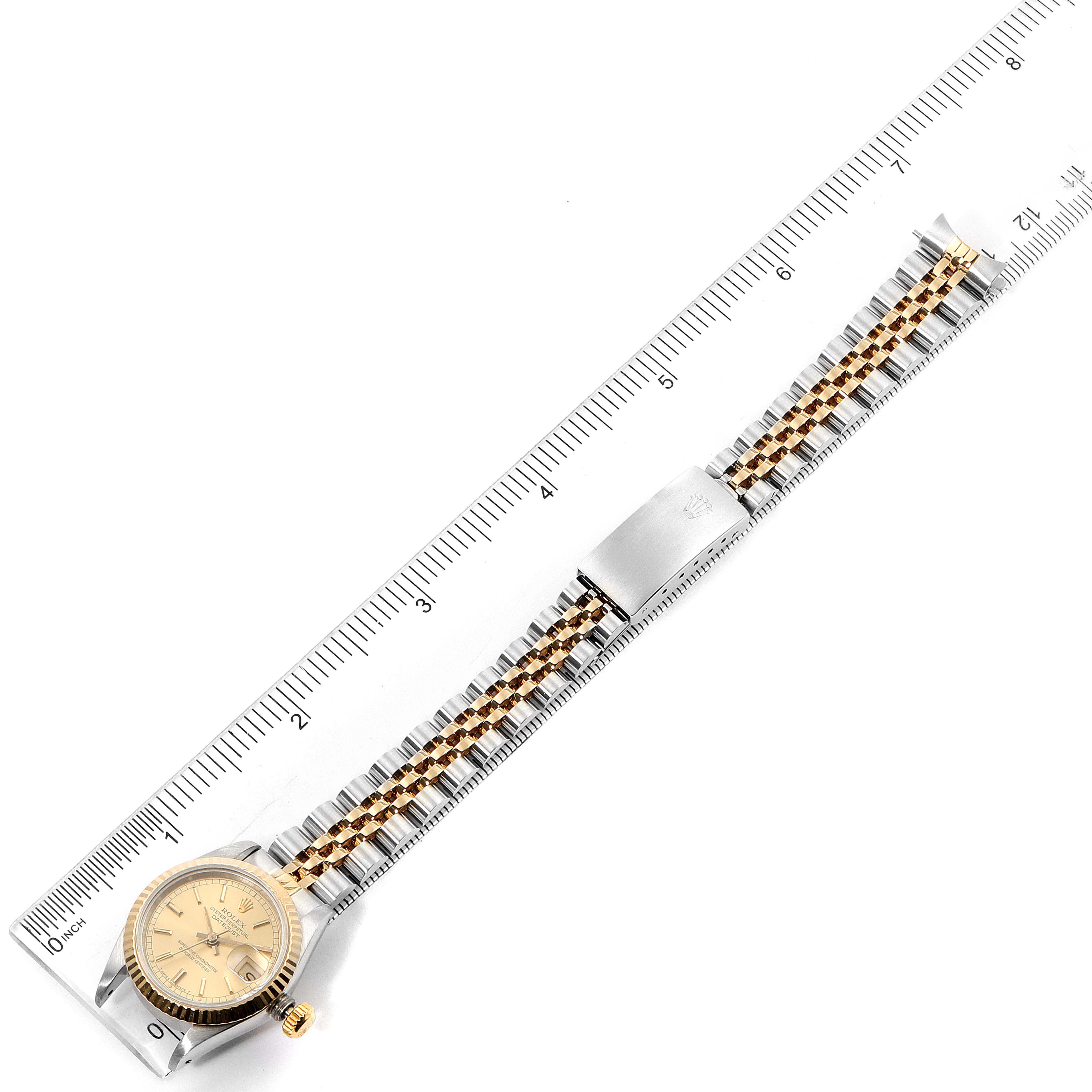 The Rolex Datejust 69173 Women's Steel and Gold (two tone) Champagne Dial 69173 Women's Steel and Gold (two tone) Champagne Dial watch is shown from a top-down angle alongside a ruler, highlighting its face, bezel, and bracelet.