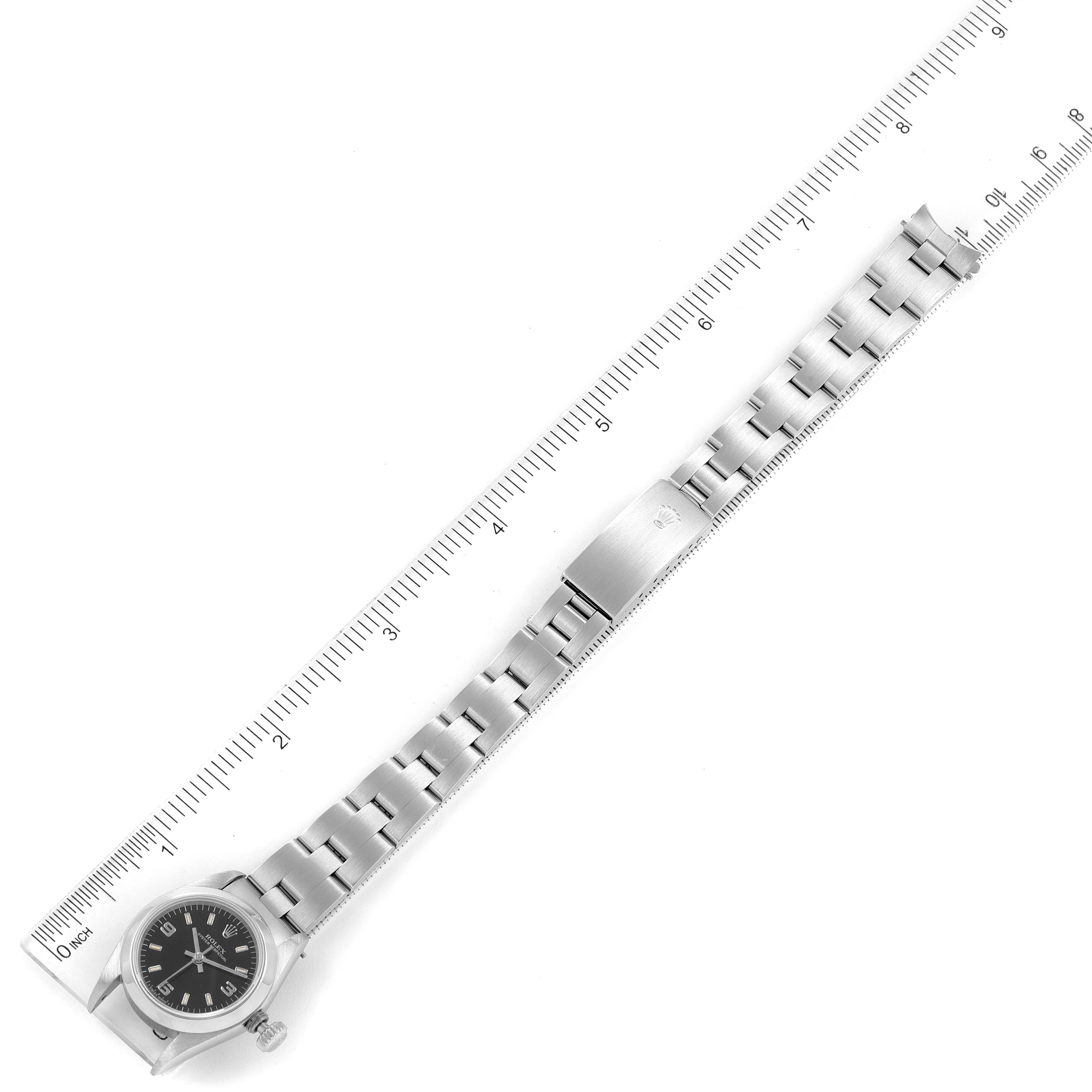 The image shows a top-down view of a Rolex Oyster Perpetual 67180 Women's Stainless Steel Black Dial 67180 Women's Stainless Steel Black Dial watch with its full metal bracelet and a ruler for scale.