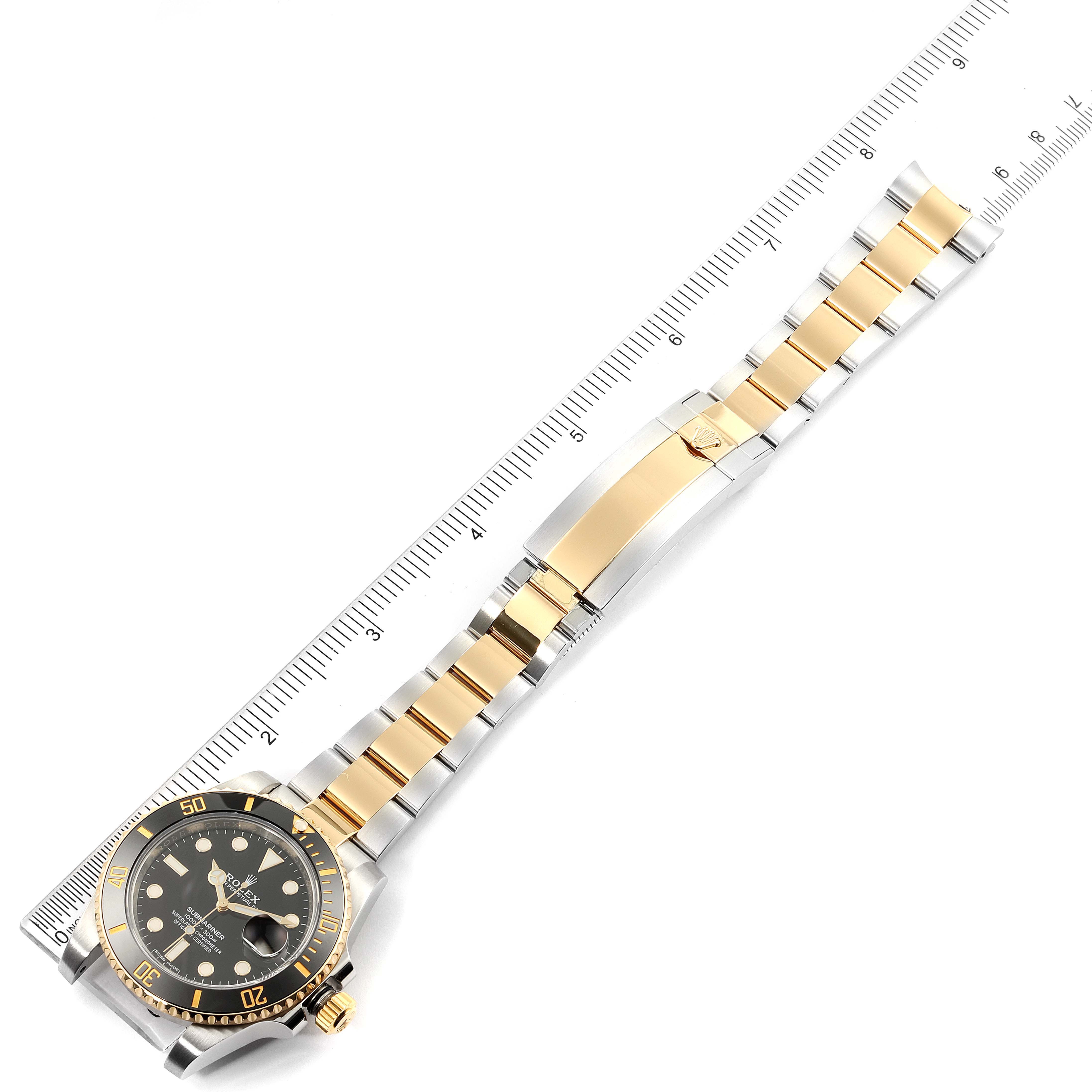 The image shows a Rolex Submariner 116613 Men's Steel and Gold (two tone) Black Dial 116613 Men's Steel and Gold (two tone) Black Dial watch laying flat, highlighting its black dial, gold bezel, and two-tone metal bracelet placed next to a ruler.