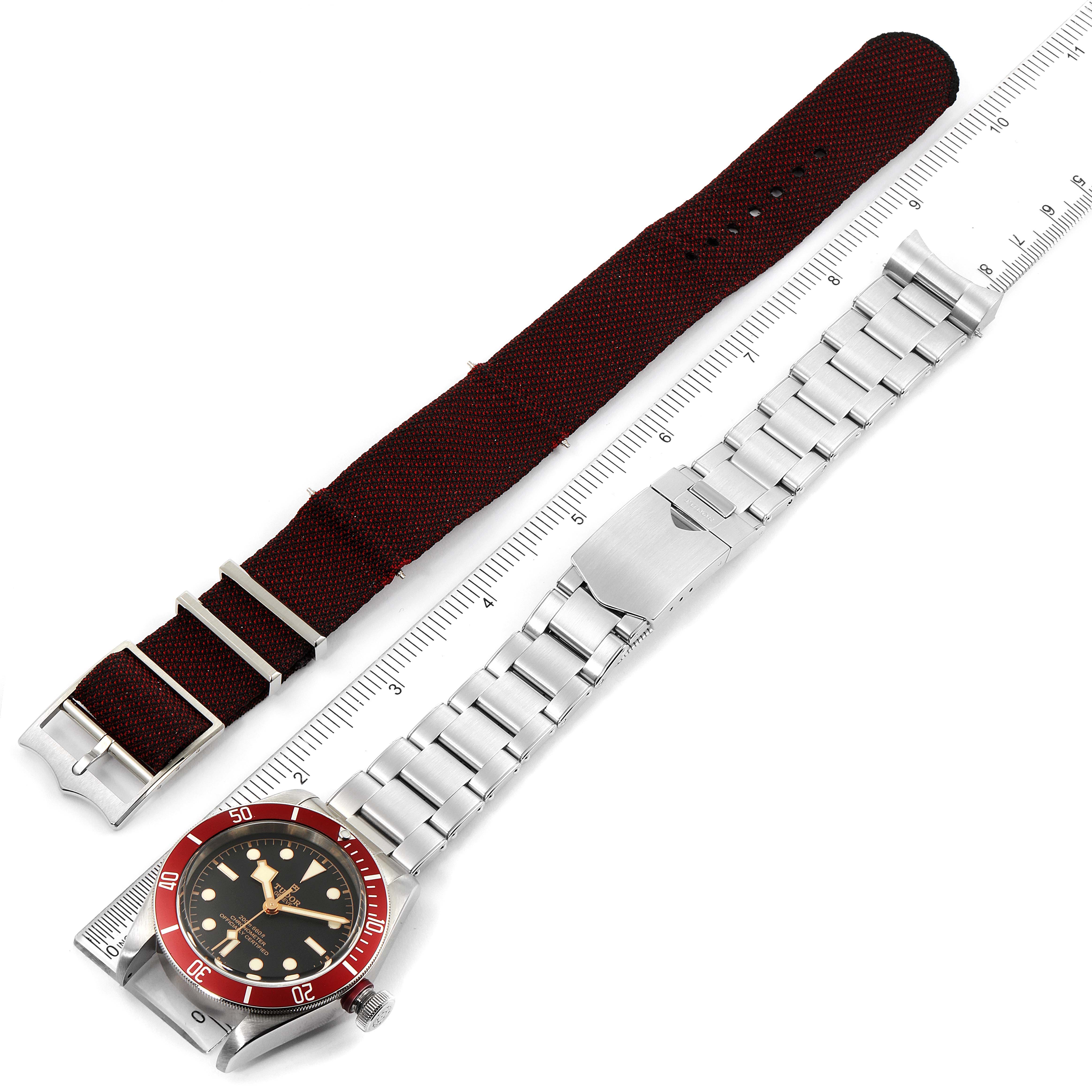 This image shows the Tudor Heritage Black Bay 79230R Men
s Stainless Steel Black Dial 79230R Men
s Stainless Steel Black Dial watch with a metal bracelet and a separate fabric strap, displayed alongside a ruler.