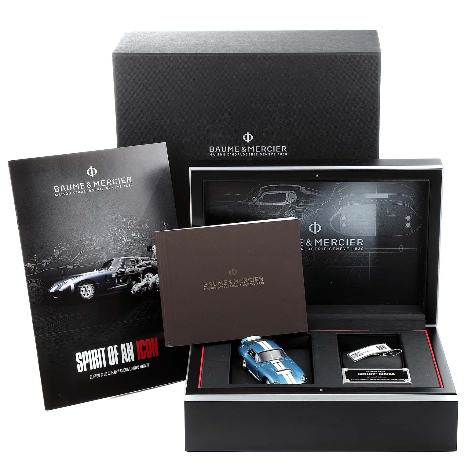 The image shows a boxed set of Baume & Mercier Clifton M0A10343 Men's Stainless Steel Blue Dial M0A10343 Men's Stainless Steel Blue Dial watch accessories, including a booklet, a miniature car, and other items.