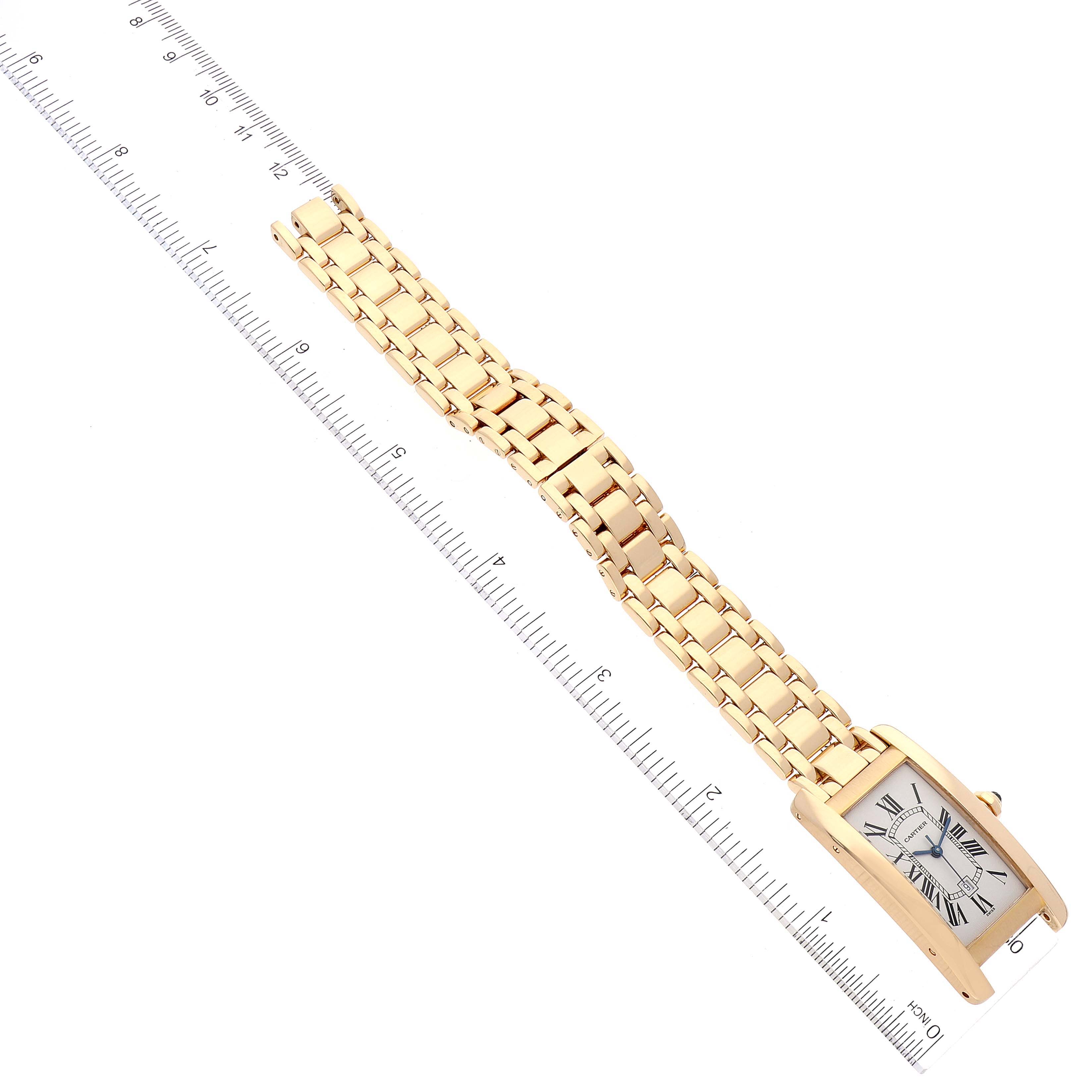 The image shows a Cartier Tank Americaine W26035K2 Women's Yellow Gold Silver Dial W26035K2 Women's Yellow Gold Silver Dial watch lying flat, with a gold bracelet and part of the face visible, next to a ruler.
