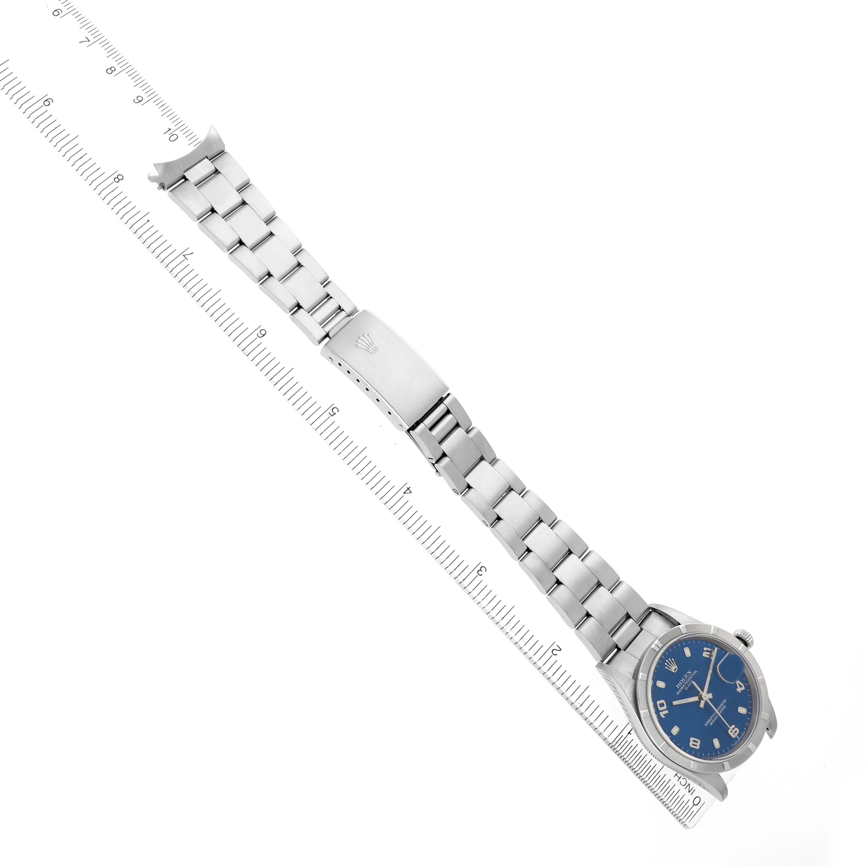 The Rolex Date 15210 Men's Stainless Steel Blue Dial watch is shown from a top view, displaying the bracelet, clasp, and blue dial with a ruler alongside for scale.