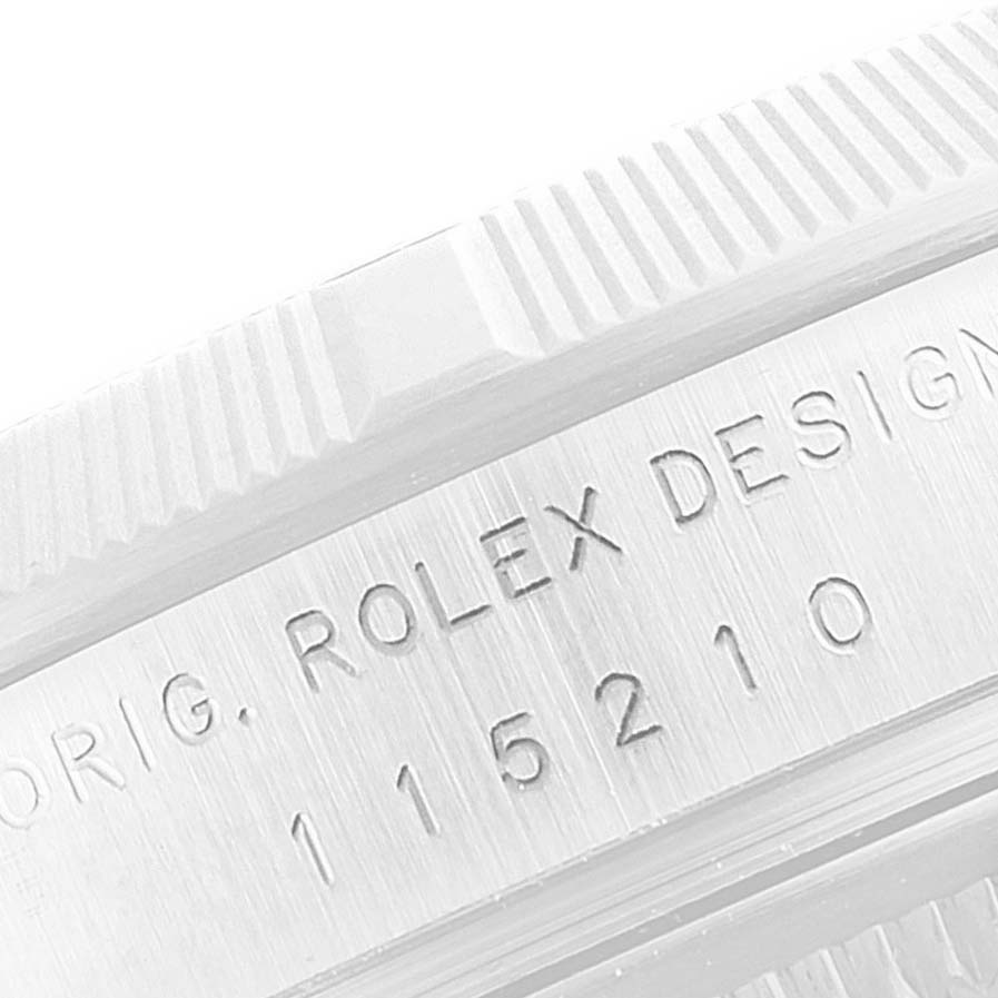 Close-up of a Rolex Date 115210 Men's Stainless Steel Blue Dial 115210 Men's Stainless Steel Blue Dial model showing the engraved "Rolex Design 115210" on the case side with part of the bezel visible.