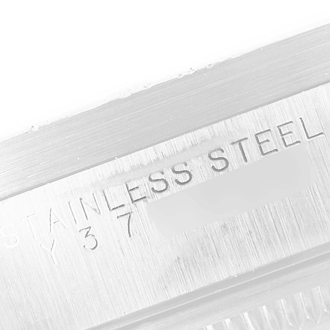 The image shows a close-up of the engraved "STAINLESS STEEL" text on a Rolex Date 15210 Men's Stainless Steel White Dial 15210 Men's Stainless Steel White Dial model watch case.
