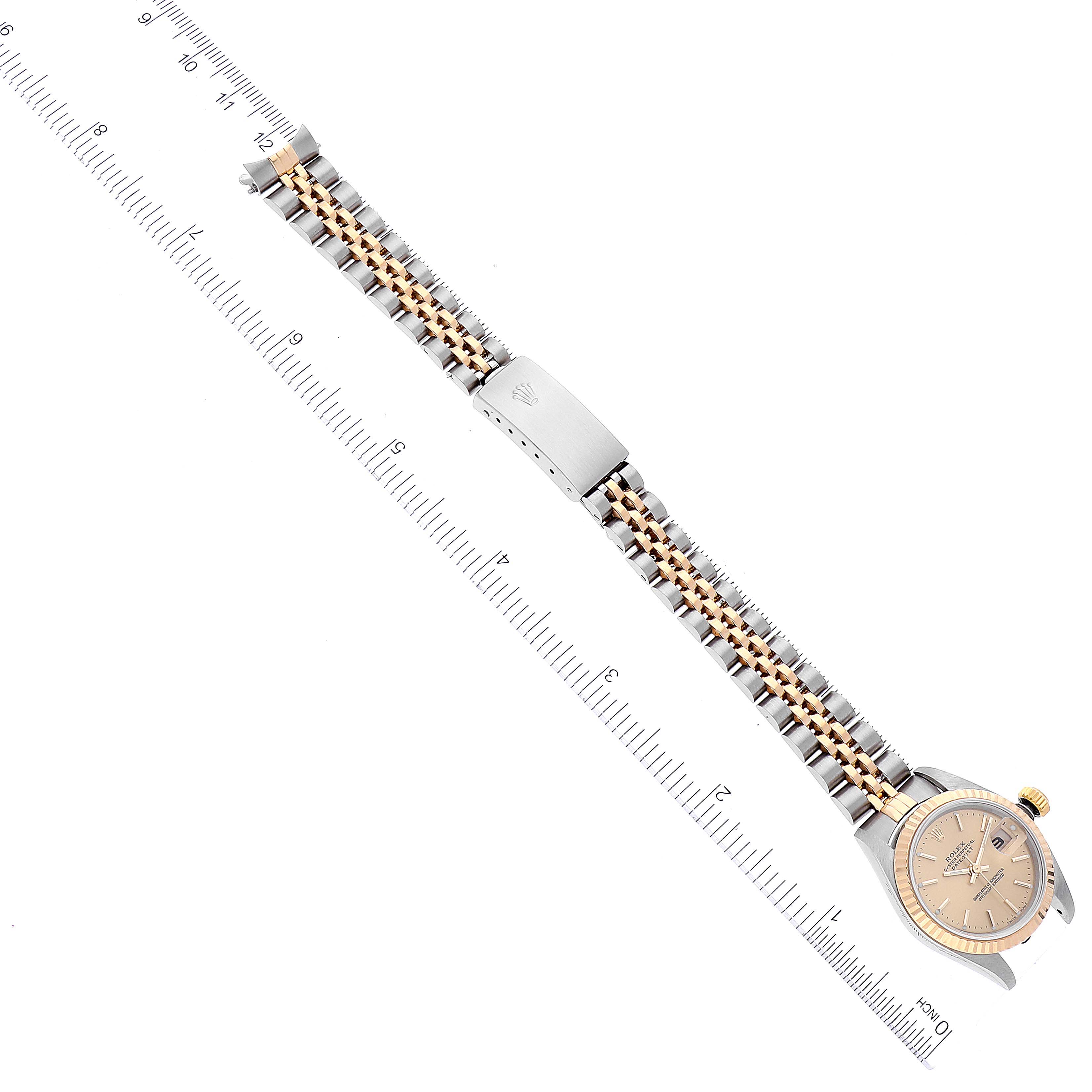 The image shows a Rolex Datejust 79173 Women's Steel and Gold (two tone) Champagne Dial 79173 Women's Steel and Gold (two tone) Champagne Dial watch from a top-down angle, highlighting its dial, bezel, and two-tone bracelet alongside a measuring ruler.