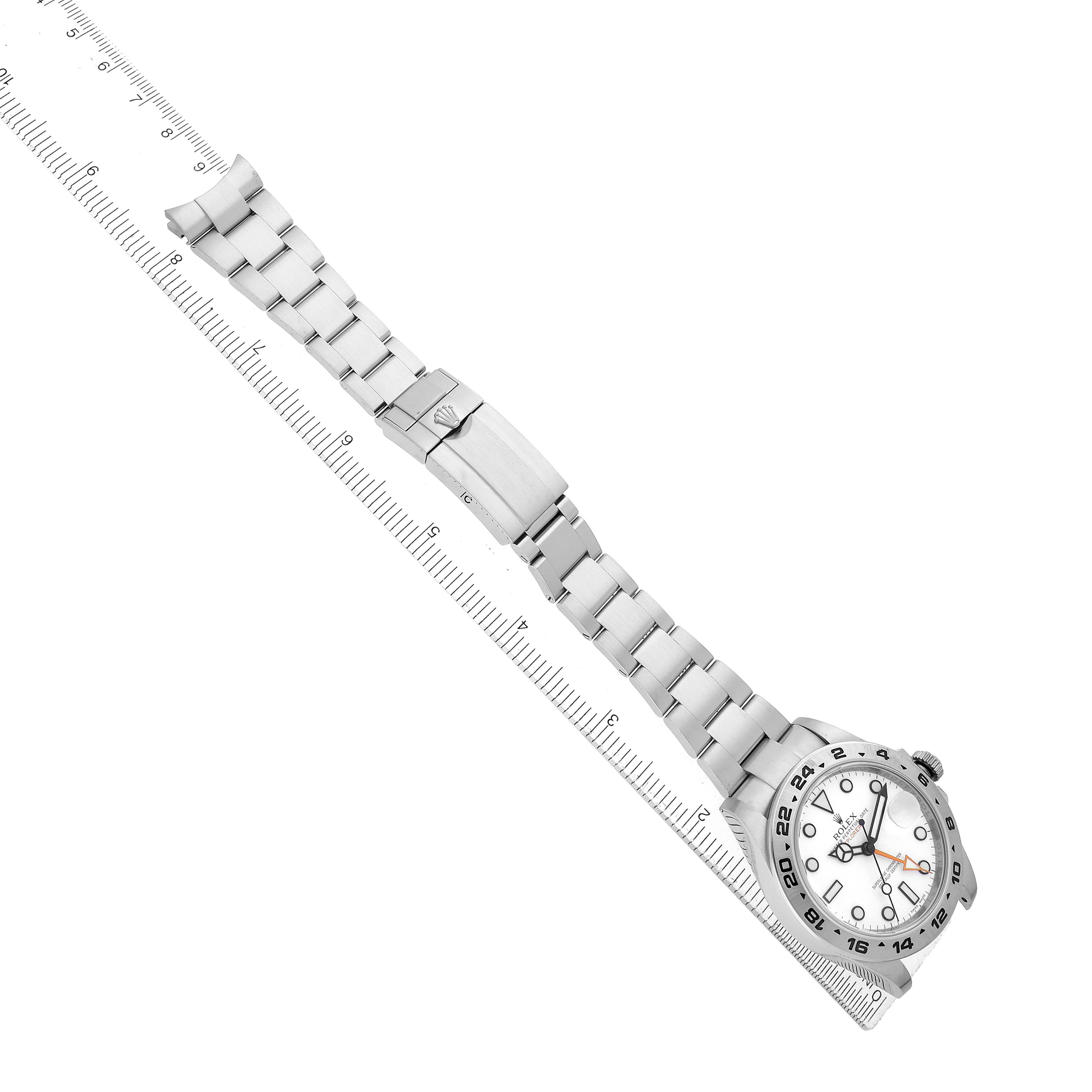 The image shows a Rolex Explorer 216570 Men's Stainless Steel White Dial watch at a diagonal angle, highlighting the bracelet, clasp, and face, alongside a measuring ruler.