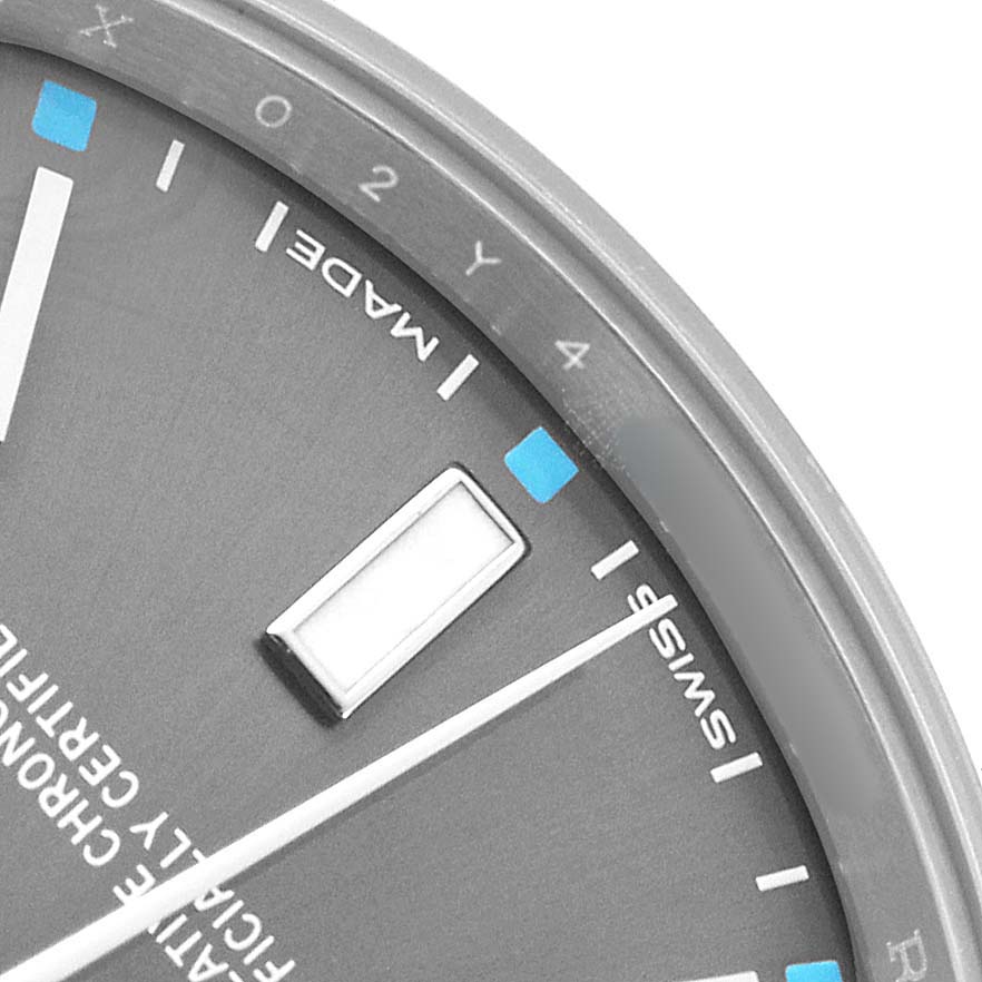 The image shows a partial view of the dial and bezel of a Rolex Oyster Perpetual 114300 Men's Stainless Steel Grey Dial watch, highlighting index markers and text details.