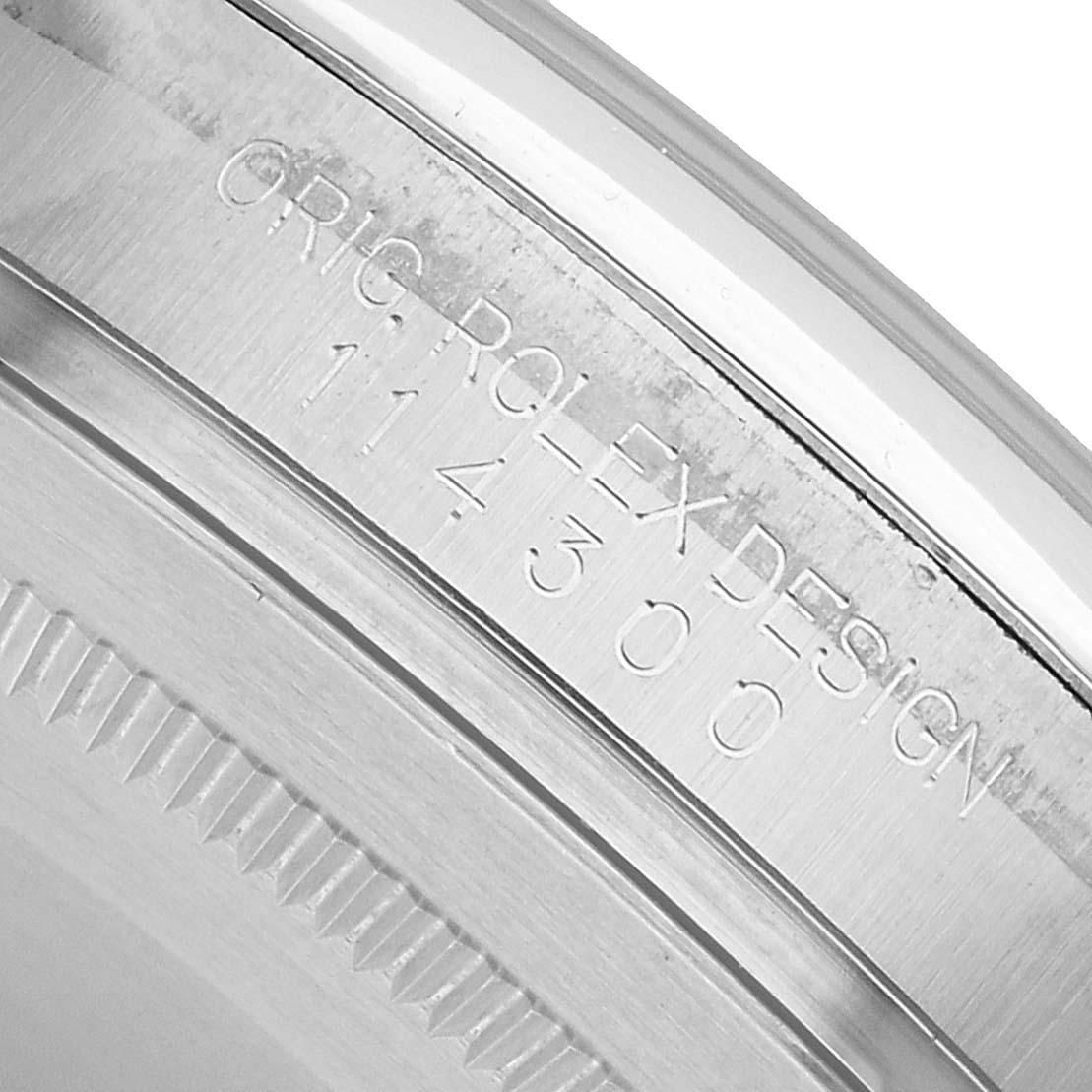 The image shows a close-up of the case engraving on a Rolex Oyster Perpetual 114300 Men's Stainless Steel Grey Dial watch, detailing the model number.