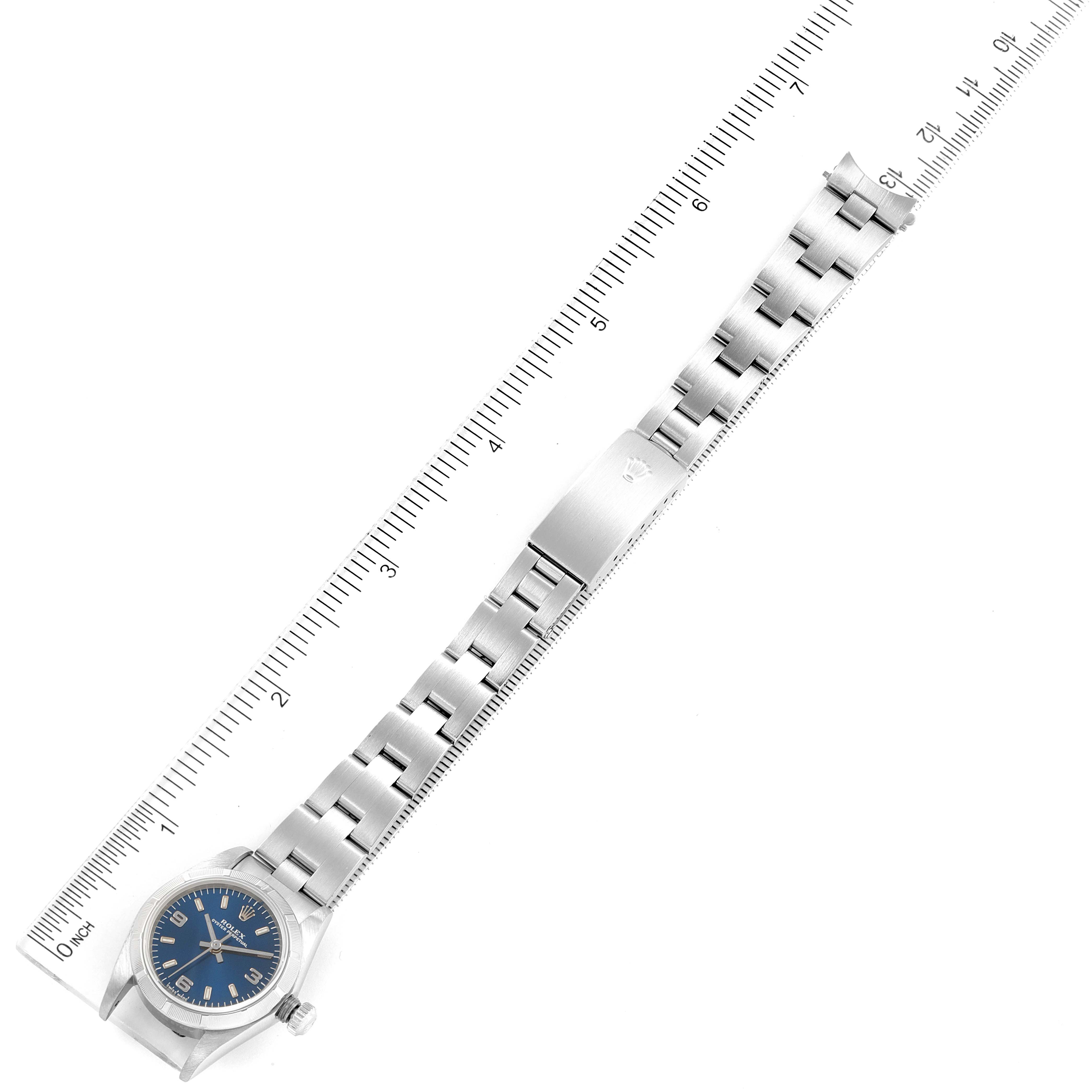 The image shows the entire Rolex Oyster Perpetual 76030 Women
s Stainless Steel Blue Dial 76030 Women
s Stainless Steel Blue Dial watch, including its face, bracelet, and clasp, positioned alongside a ruler.