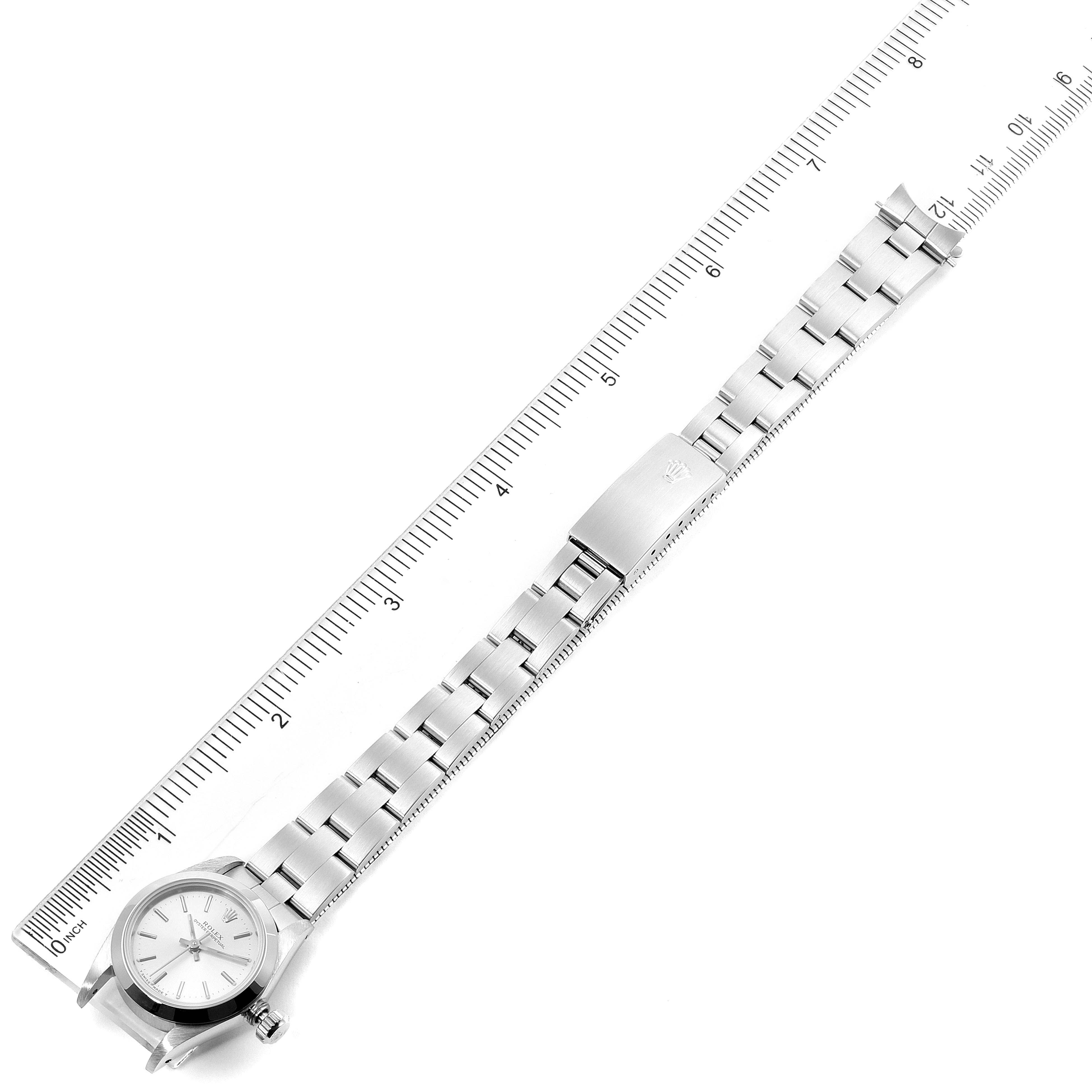 This image shows a top-down view of a Rolex Oyster Perpetual 67180 Women's Stainless Steel Silver Dial 67180 Women's Stainless Steel Silver Dial watch, displaying its face, bracelet, and clasp alongside a ruler.