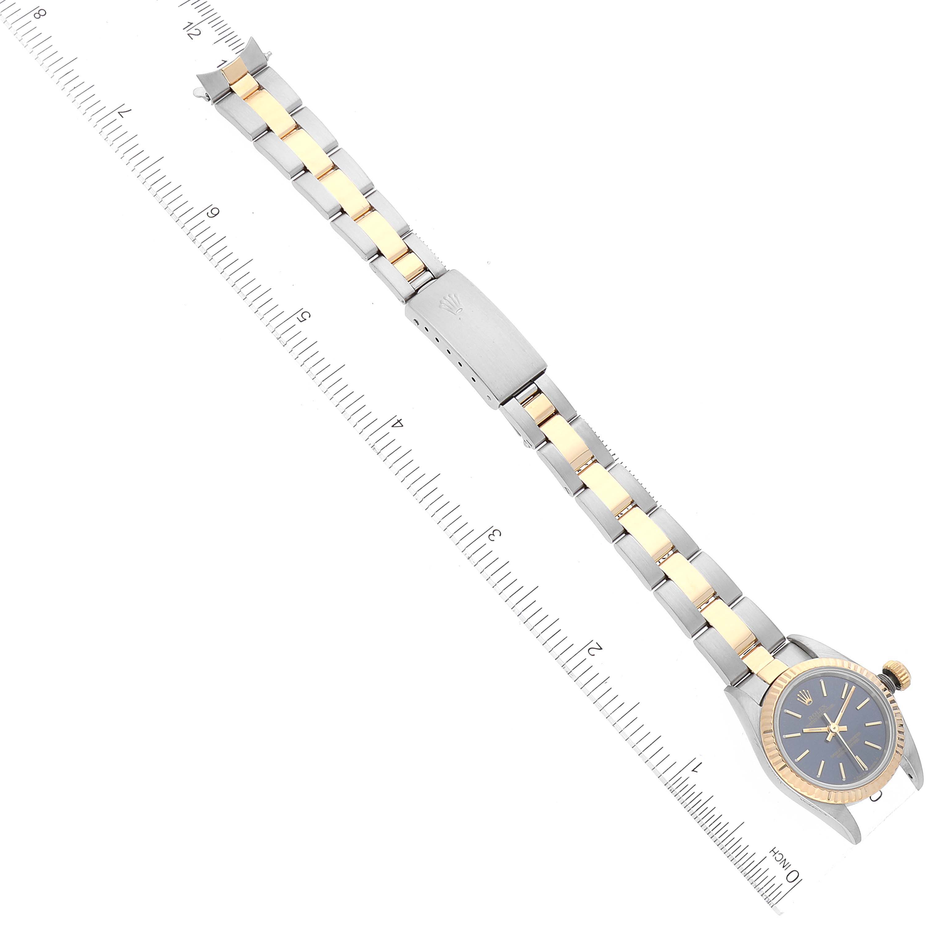 The Rolex Oyster Perpetual 67193 Women's Steel and Gold (two tone) Blue Dial 67193 Women's Steel and Gold (two tone) Blue Dial watch is shown laid flat with a ruler, displaying its blue dial and two-tone bracelet.