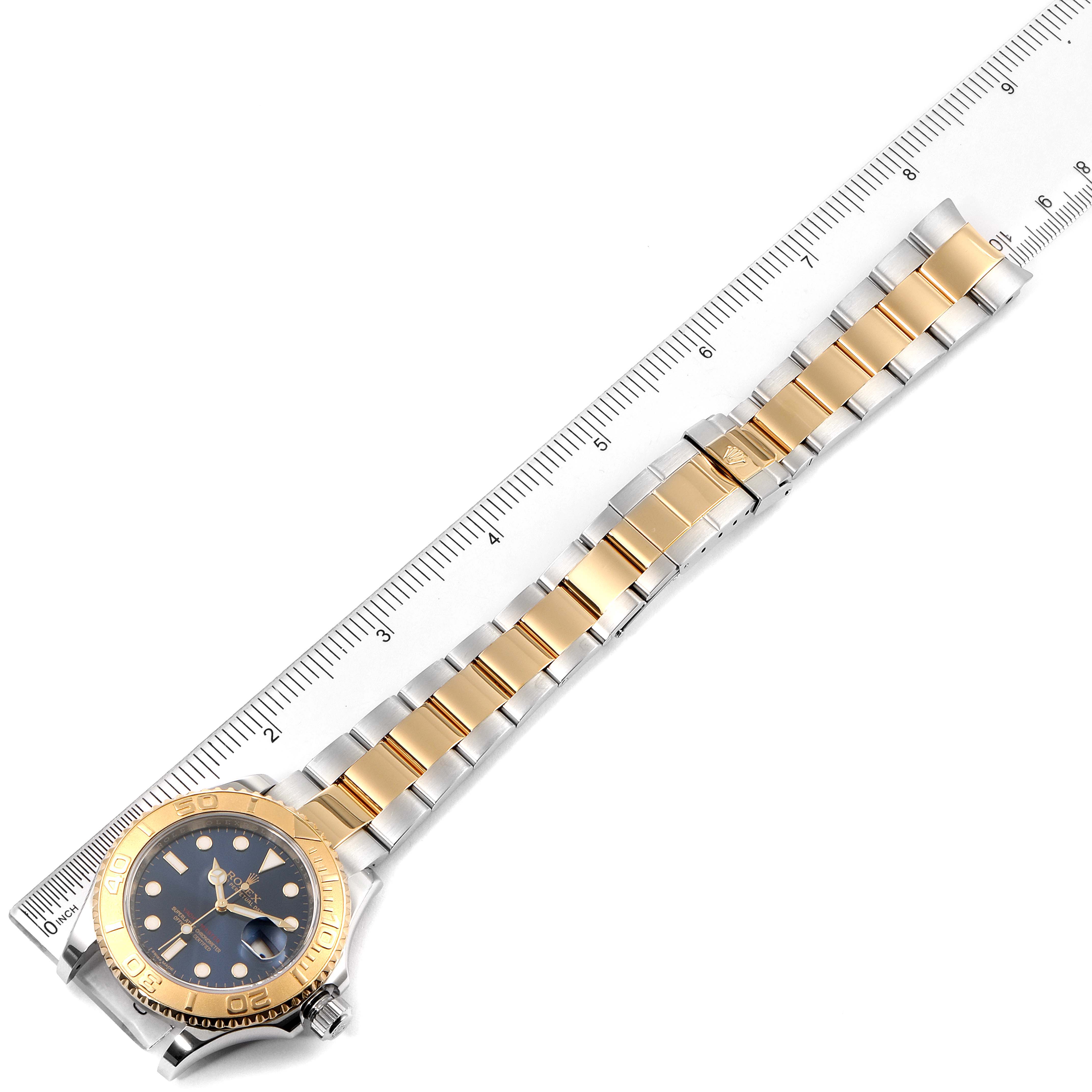 The Rolex Yacht-Master 16623 Men's Steel and Gold (two tone) Blue Dial 16623 Men's Steel and Gold (two tone) Blue Dial watch is shown from an overhead angle, displaying the entire watch face and bracelet against a ruler backdrop.