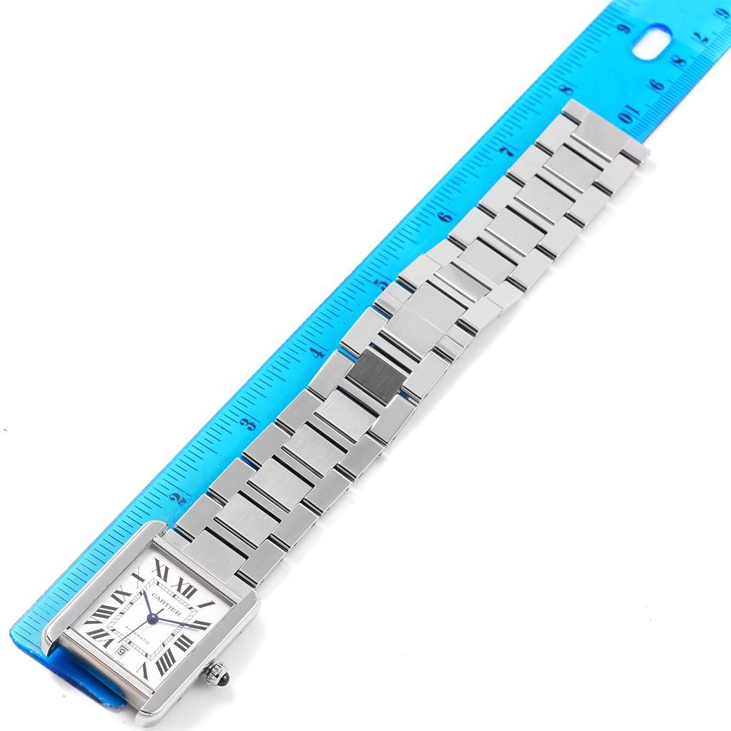 The Tank Obus model by Cartier is shown from its side, displaying the face, crown, and metal bracelet band next to a blue ruler.