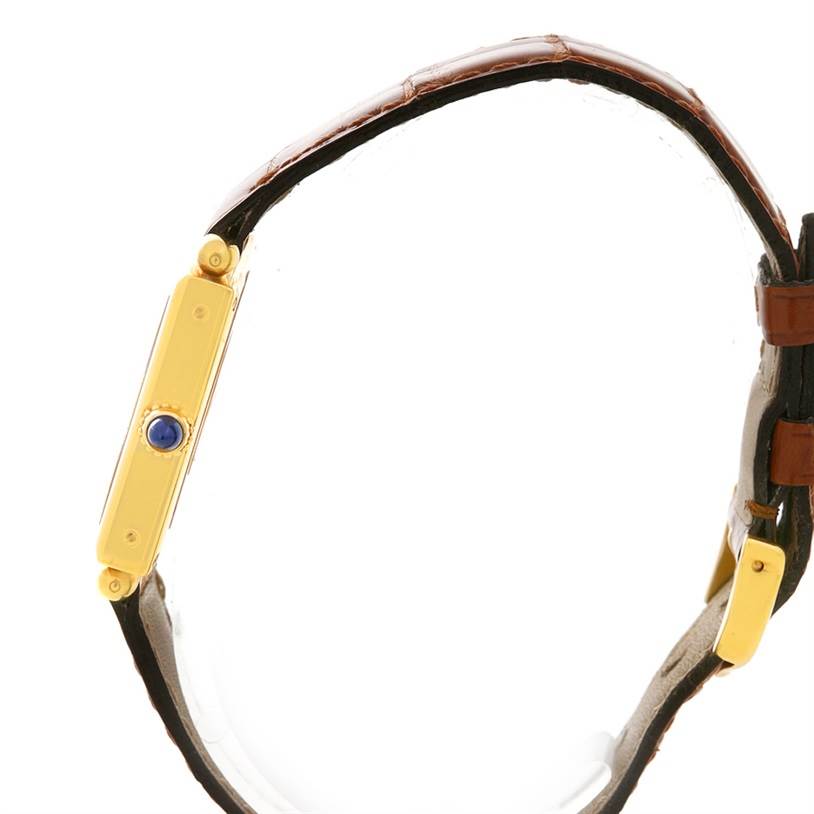 The image shows a side view of the Cartier Tank Obus W1512256 Yellow Gold Silver Dial W1512256 Yellow Gold Silver Dial watch, highlighting its slim profile, gold casing, and blue cabochon crown.