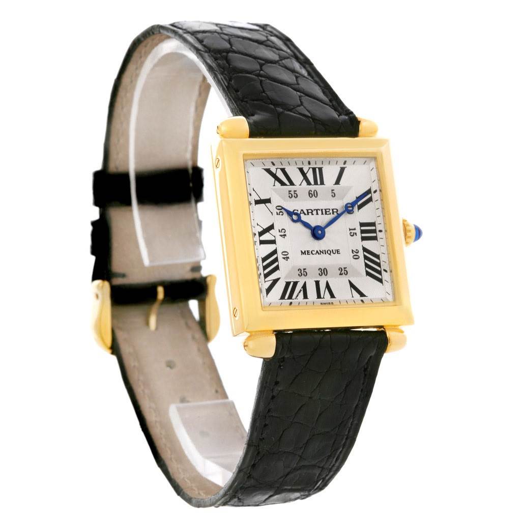 The Cartier Tank Obus W1527551 Men's Yellow Gold Silver Dial W1527551 Men's Yellow Gold Silver Dial model watch is shown at a 3/4 angle, displaying its rectangular face, Roman numerals, black strap, and gold casing.