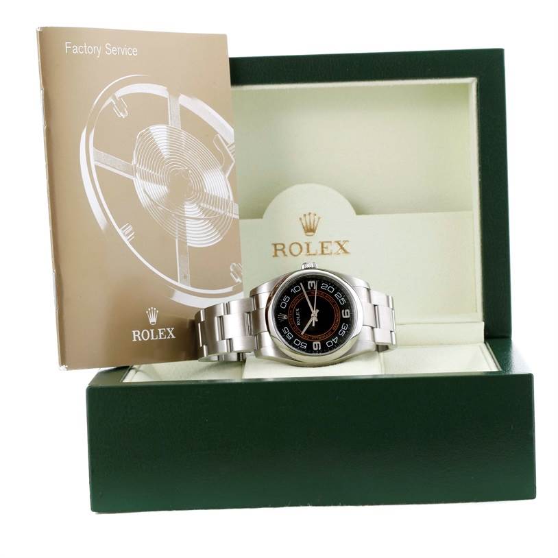 This image features a Rolex Oyster Perpetual 116000 Men
s Stainless Steel Black Dial 116000 Men
s Stainless Steel Black Dial watch displayed in an open green box with a factory service booklet beside it.