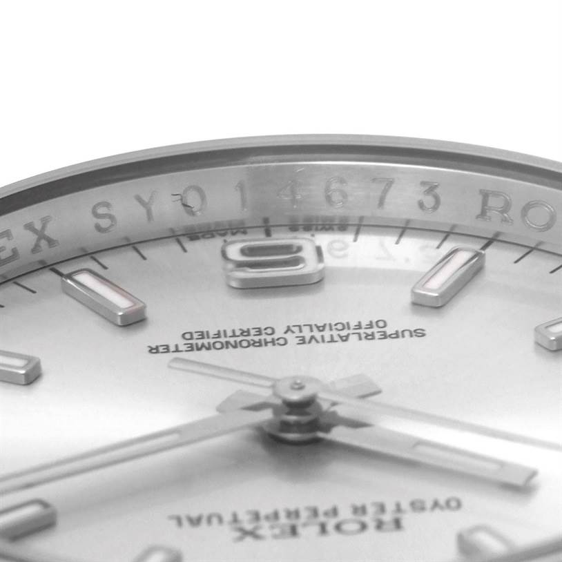 This close-up angle of the Rolex Oyster Perpetual 116000 Men's Stainless Steel Silver Dial 116000 Men's Stainless Steel Silver Dial watch shows the dial, hour markers, and the engraving on the inner bezel.