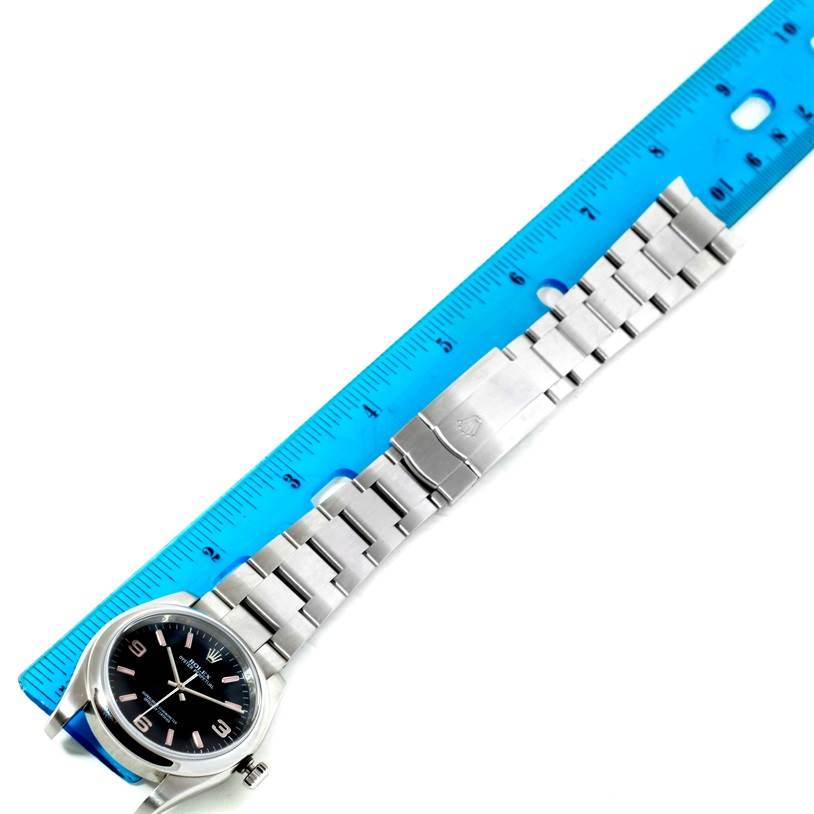 The image shows a Rolex Oyster Perpetual 116000 Men's Stainless Steel Black Dial 116000 Men's Stainless Steel Black Dial watch laid flat alongside a ruler, displaying the face and bracelet in a top-down view.