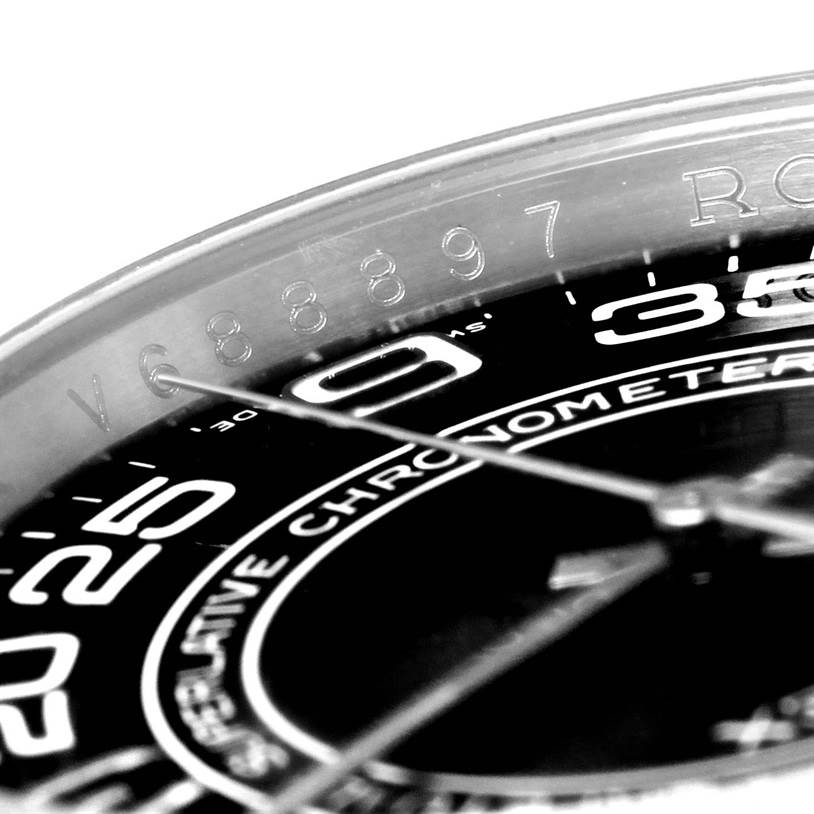 This close-up image of the Rolex Oyster Perpetual 116000 Men's Stainless Steel Black Dial 116000 Men's Stainless Steel Black Dial watch shows part of the dial, the chapter ring, and the serial number engraved on the inner bezel.