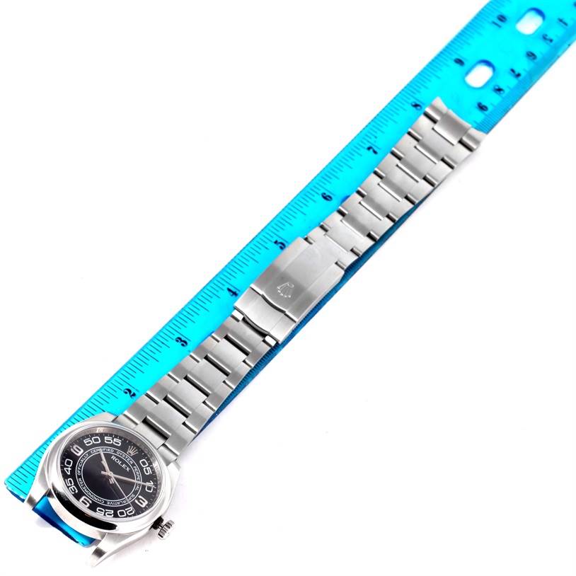 The image shows a Rolex Oyster Perpetual 116000 Men's Stainless Steel Black Dial 116000 Men's Stainless Steel Black Dial watch laid flat against a ruler, highlighting the bracelet and clasp.