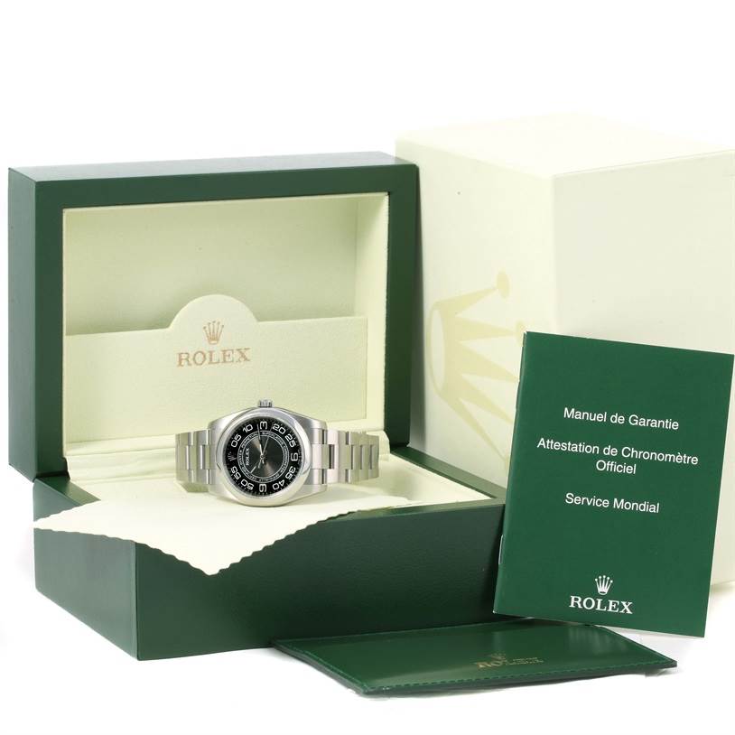 The Rolex Oyster Perpetual 116000 Men's Stainless Steel Black Dial 116000 Men's Stainless Steel Black Dial watch is displayed front-facing in an open box with accompanying booklets and documents.