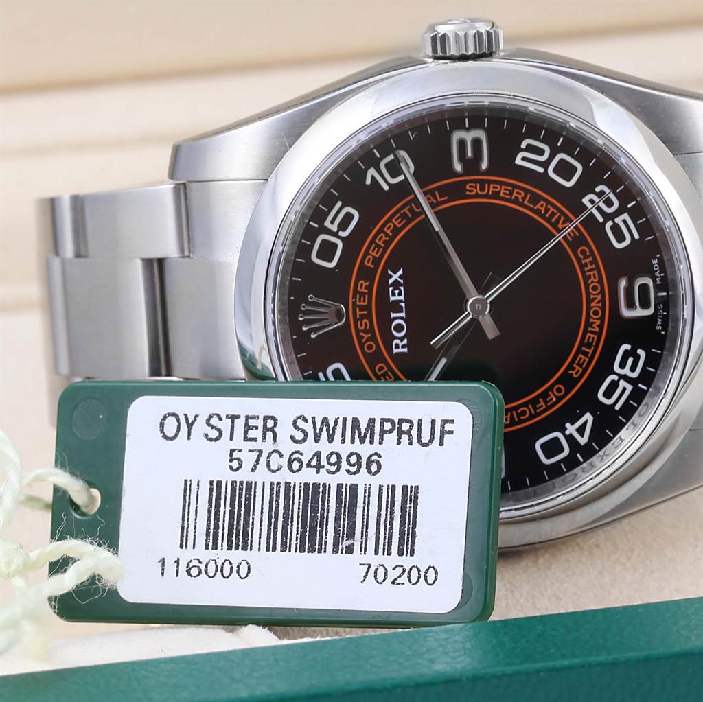 The image shows a close-up of a Rolex Oyster Perpetual 116000 Men's Stainless Steel Black Dial 116000 Men's Stainless Steel Black Dial watch face and bezel, along with a tag and part of the metal bracelet.