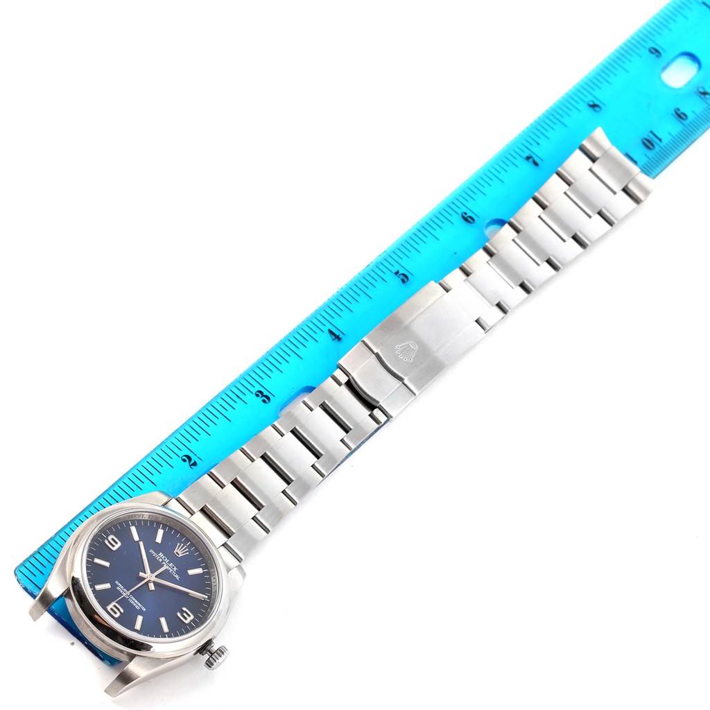 The image shows a top-view angle of a Rolex Oyster Perpetual 116000 Men's Blue Dial 116000 Men's Blue Dial watch and its metal bracelet next to a blue ruler.