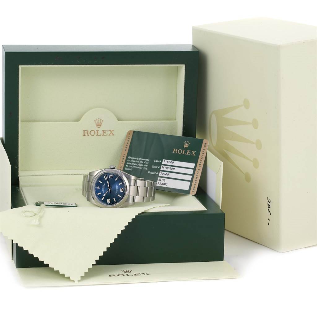 The Rolex Oyster Perpetual 116000 Men's Blue Dial 116000 Men's Blue Dial watch is shown in its case with the warranty card visible, viewed from a front angle.
