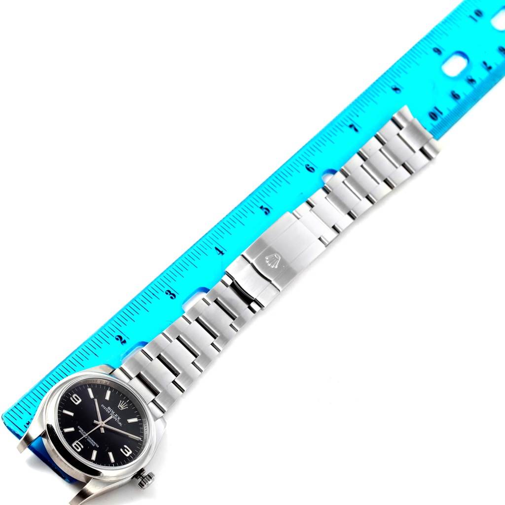 This overhead view showcases the Rolex Oyster Perpetual 116000 Men's Stainless Steel Black Dial 116000 Men's Stainless Steel Black Dial watch, focusing on the dial, bezel, bracelet, and clasp next to a blue ruler.