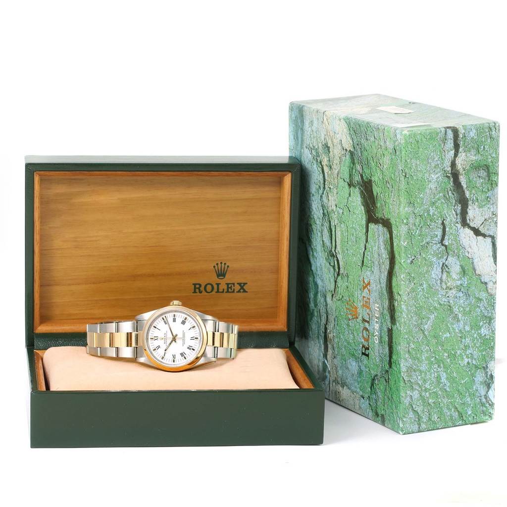 The image shows a Rolex Oyster Perpetual 14203 Men
s Steel and Gold (two tone) White Dial 14203 Men
s Steel and Gold (two tone) White Dial watch displayed in an open green and wooden box, with its outer packaging beside it.
