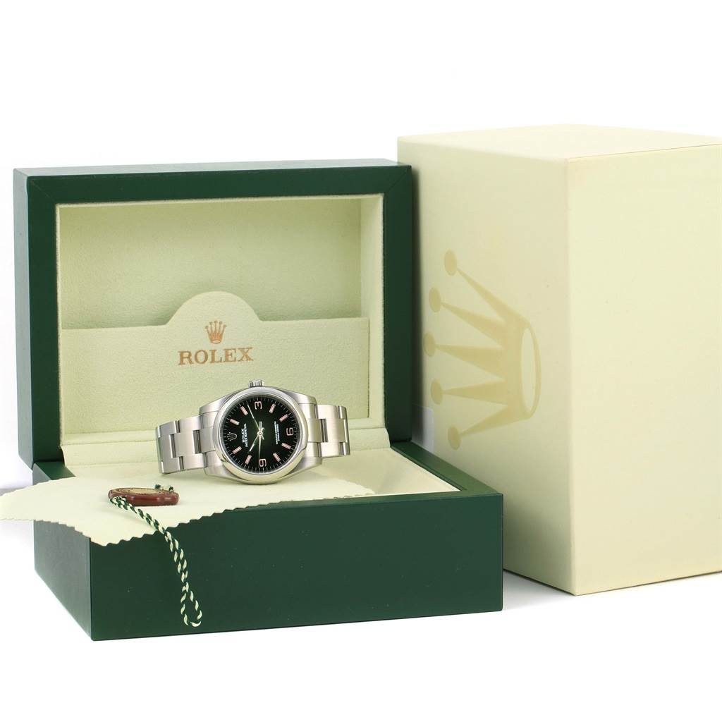 The Rolex Oyster Perpetual 116000 Men's Stainless Steel Black Dial 116000 Men's Stainless Steel Black Dial watch is displayed at an oblique angle, inside its open box, with a visible tag and exterior packaging.