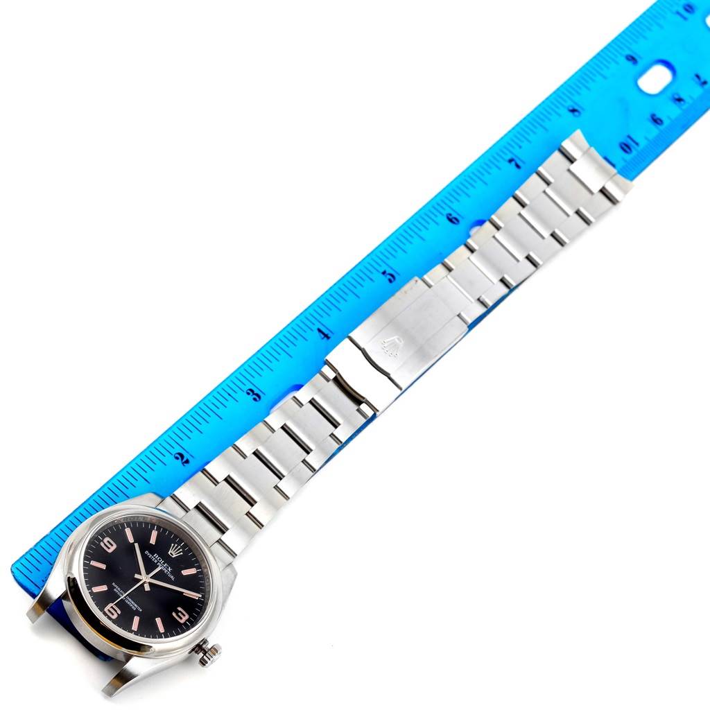 The image shows a top-down view of a Rolex Oyster Perpetual 116000 Men's Stainless Steel Black Dial 116000 Men's Stainless Steel Black Dial watch laid flat with a blue ruler beside it.