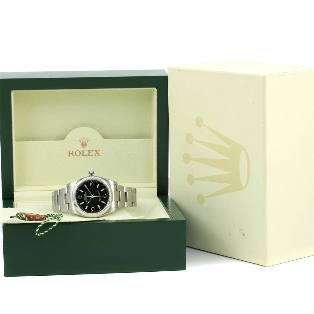 The image shows a Rolex Oyster Perpetual 116000 Men's Stainless Steel Black Dial 116000 Men's Stainless Steel Black Dial watch displayed in its open box, along with the outer packaging and a tag.