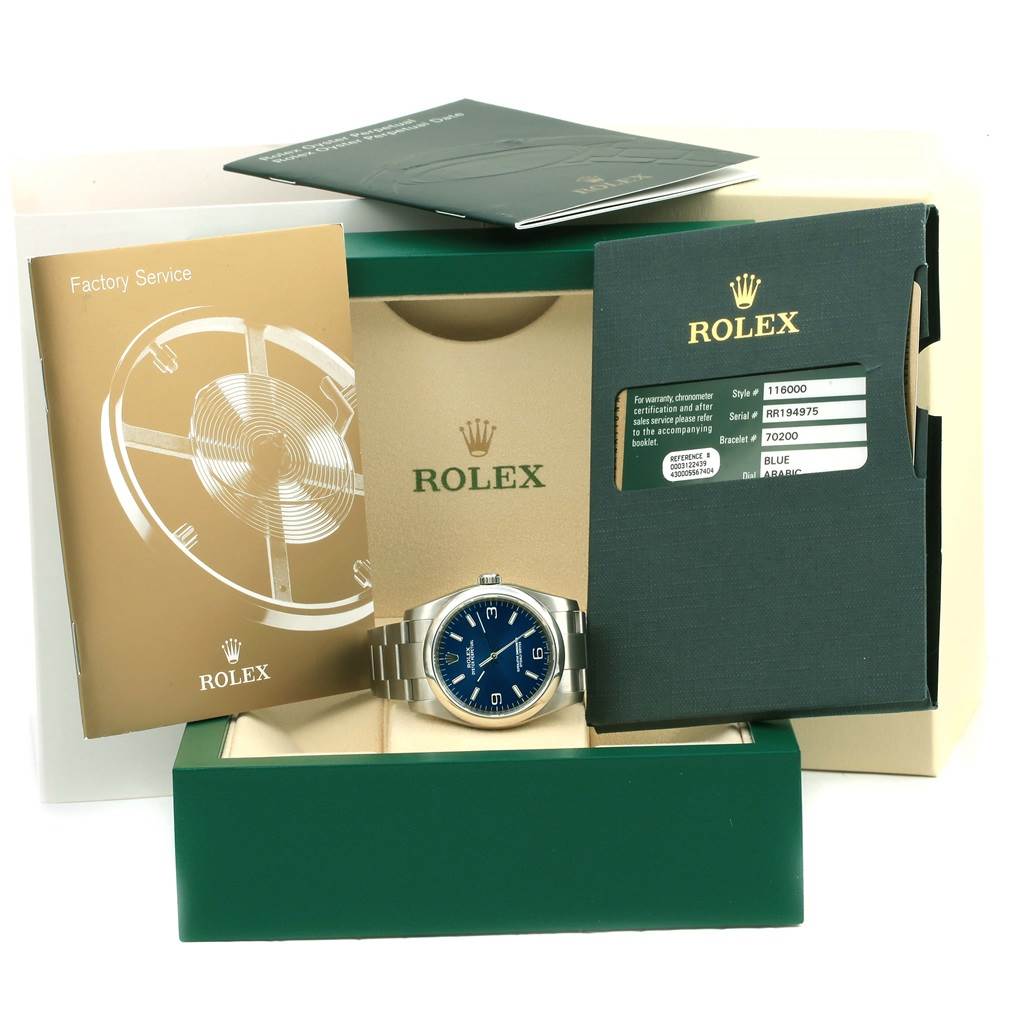 The image shows a Rolex Oyster Perpetual 116000 Men
s Stainless Steel Blue Dial 116000 Men
s Stainless Steel Blue Dial watch with a blue dial, displayed in its original packaging with accompanying documents.