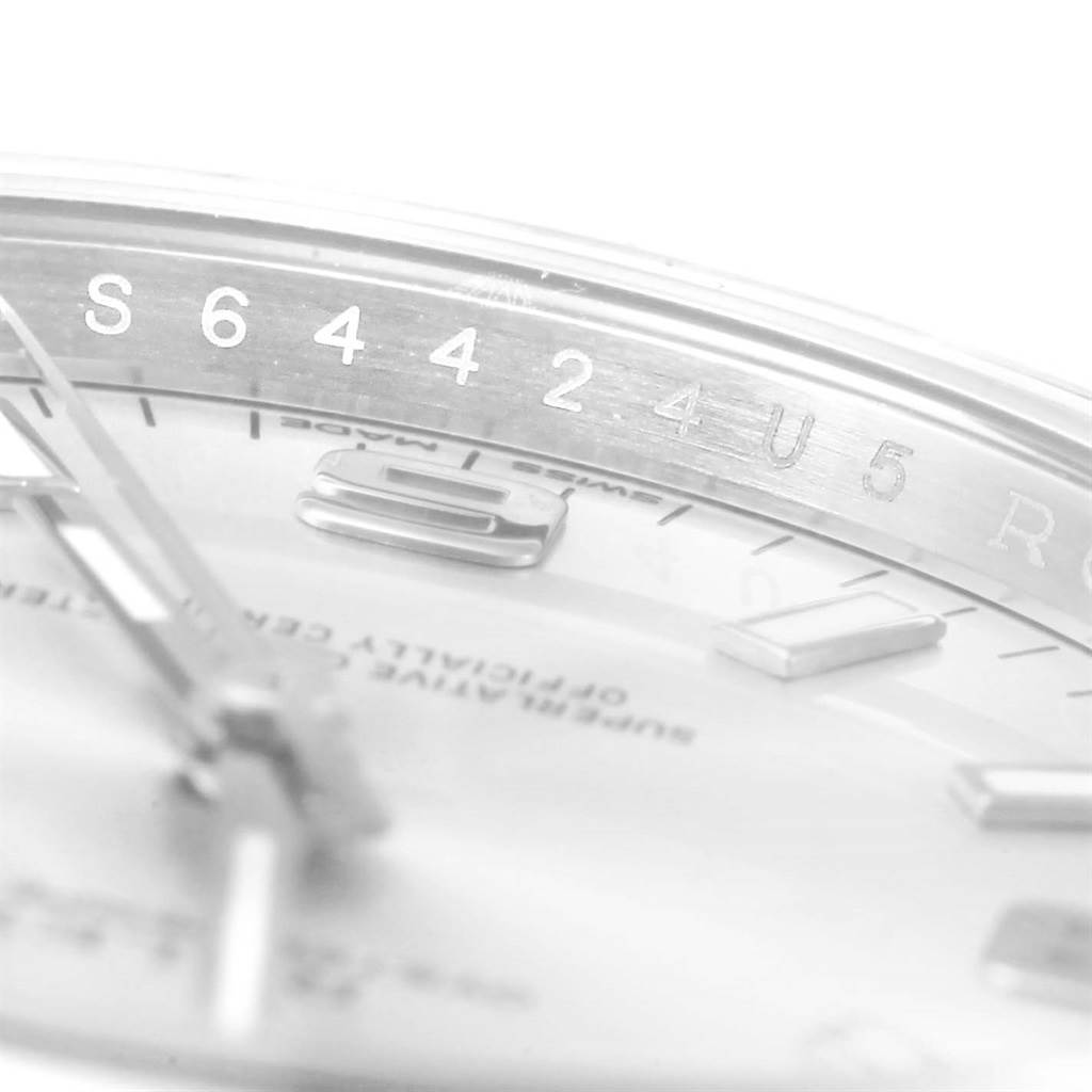 This close-up image of the Rolex Oyster Perpetual 114200 Men's Stainless Steel Silver Dial 114200 Men's Stainless Steel Silver Dial watch focuses on the dial and serial number on the inner bezel.