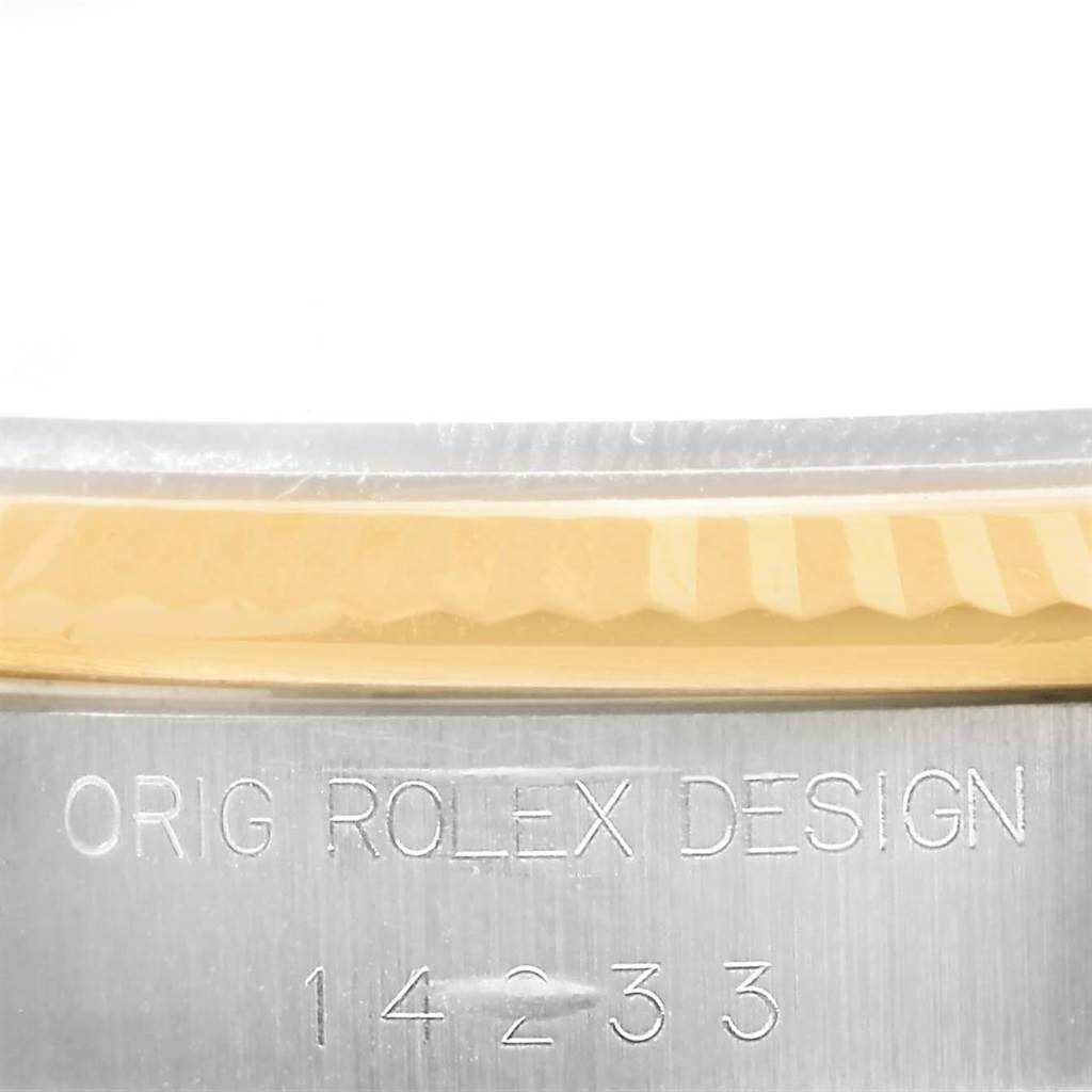 This close-up image of a Rolex Oyster Perpetual 14233 Men's Steel and Gold (two tone) Champagne Dial 14233 Men's Steel and Gold (two tone) Champagne Dial watch shows part of the bezel and the engraved serial number on the metal case.