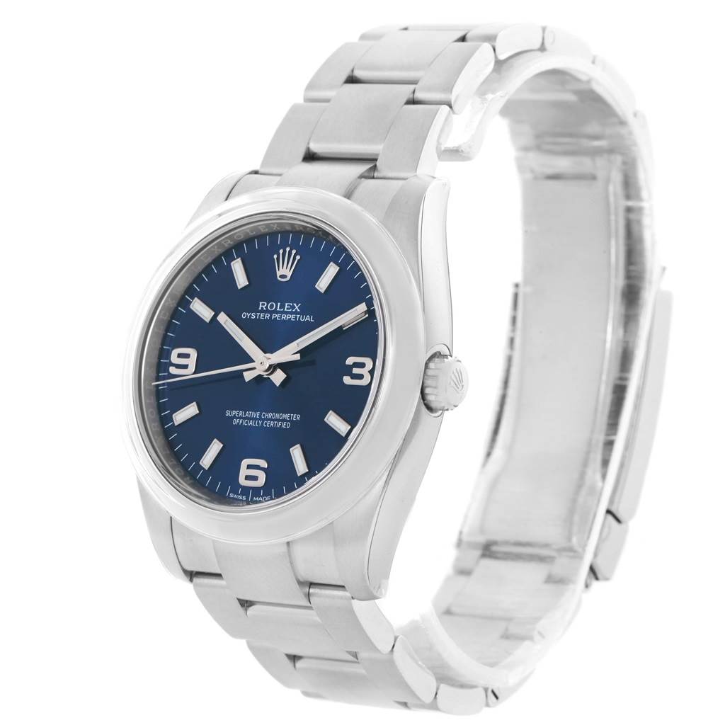 The Rolex Oyster Perpetual 114200 Stainless Steel Blue Dial 114200 Stainless Steel Blue Dial watch is shown at a three-quarter angle, highlighting the face, bezel, and partially extended bracelet.