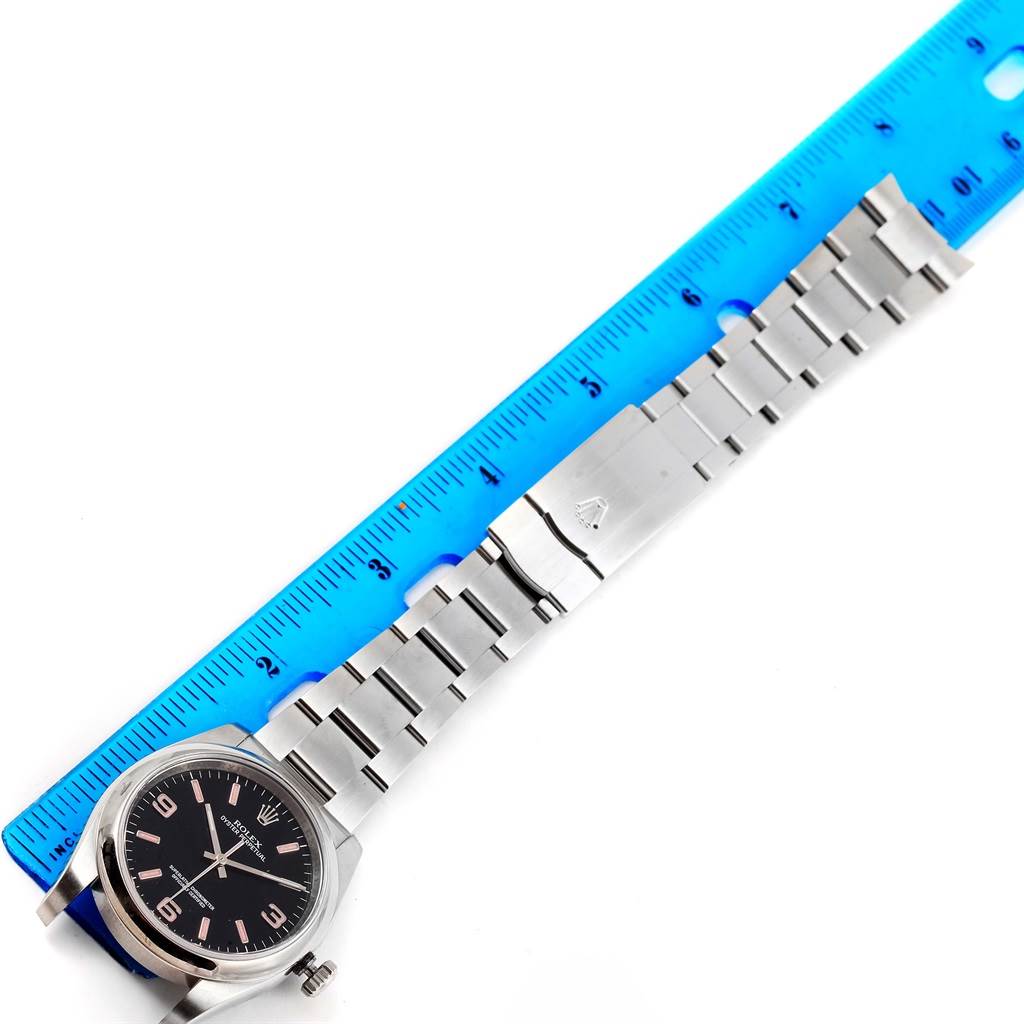 The image shows an Oyster Perpetual Rolex watch with its band fully extended next to a ruler, displaying its length.
