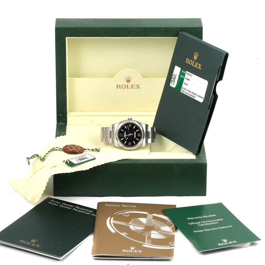 The image displays a Rolex Oyster Perpetual 116000 Men's Stainless Steel Black Dial 116000 Men's Stainless Steel Black Dial watch in its open box surrounded by booklets and tags.
