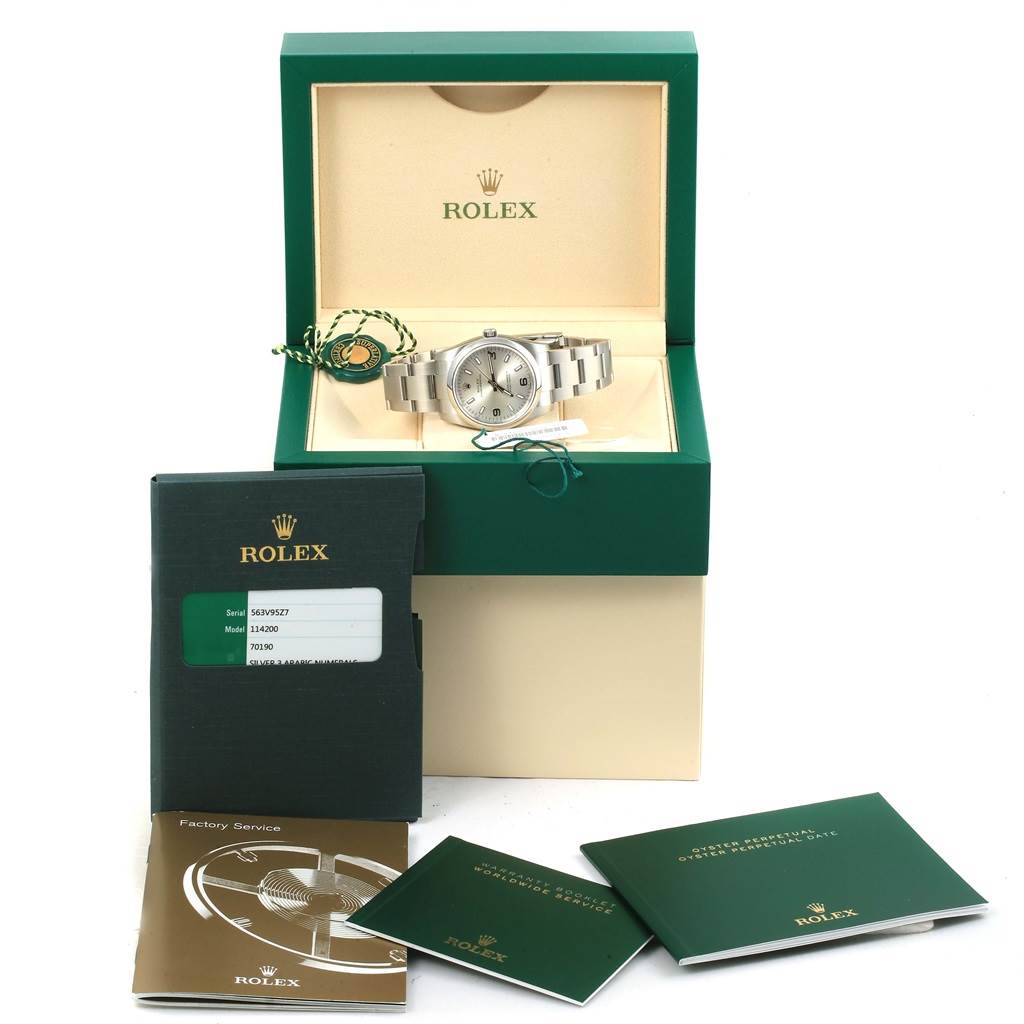 The image shows a Rolex Oyster Perpetual 114200 Men's Stainless Steel Silver Dial 114200 Men's Stainless Steel Silver Dial watch in its open box, with manuals and authentication card displayed in front.