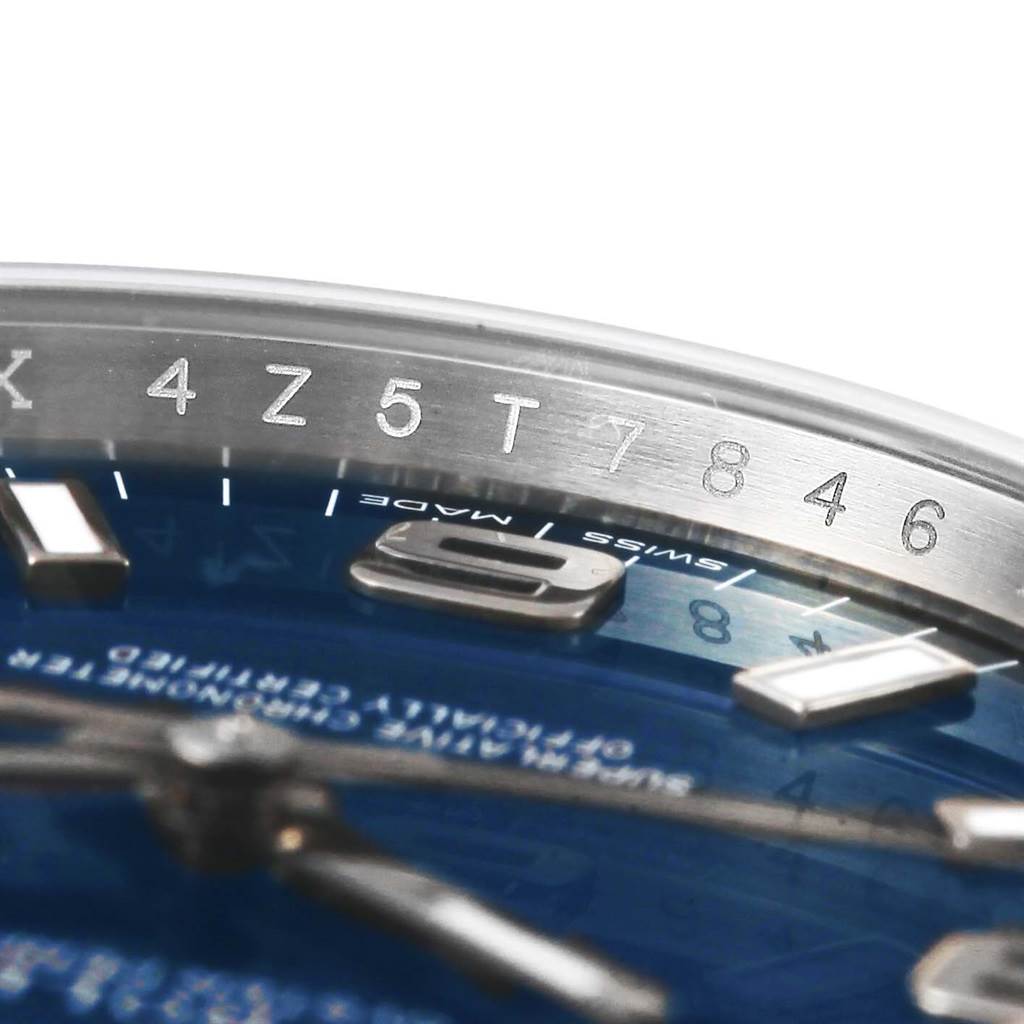 This close-up image of the Rolex Oyster Perpetual 114200 Men's Stainless Steel Blue Dial 114200 Men's Stainless Steel Blue Dial watch shows part of the dial, hour markers, and the rehaut with engraved characters.