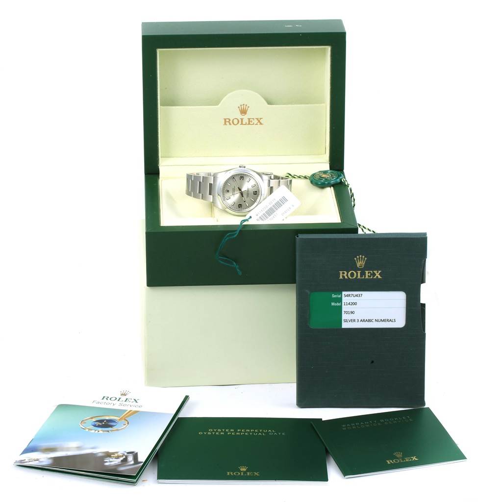 The image shows a Rolex Oyster Perpetual 114200 Men's Stainless Steel Silver Dial 114200 Men's Stainless Steel Silver Dial watch in its box, with accompanying manuals and tags displayed in front.