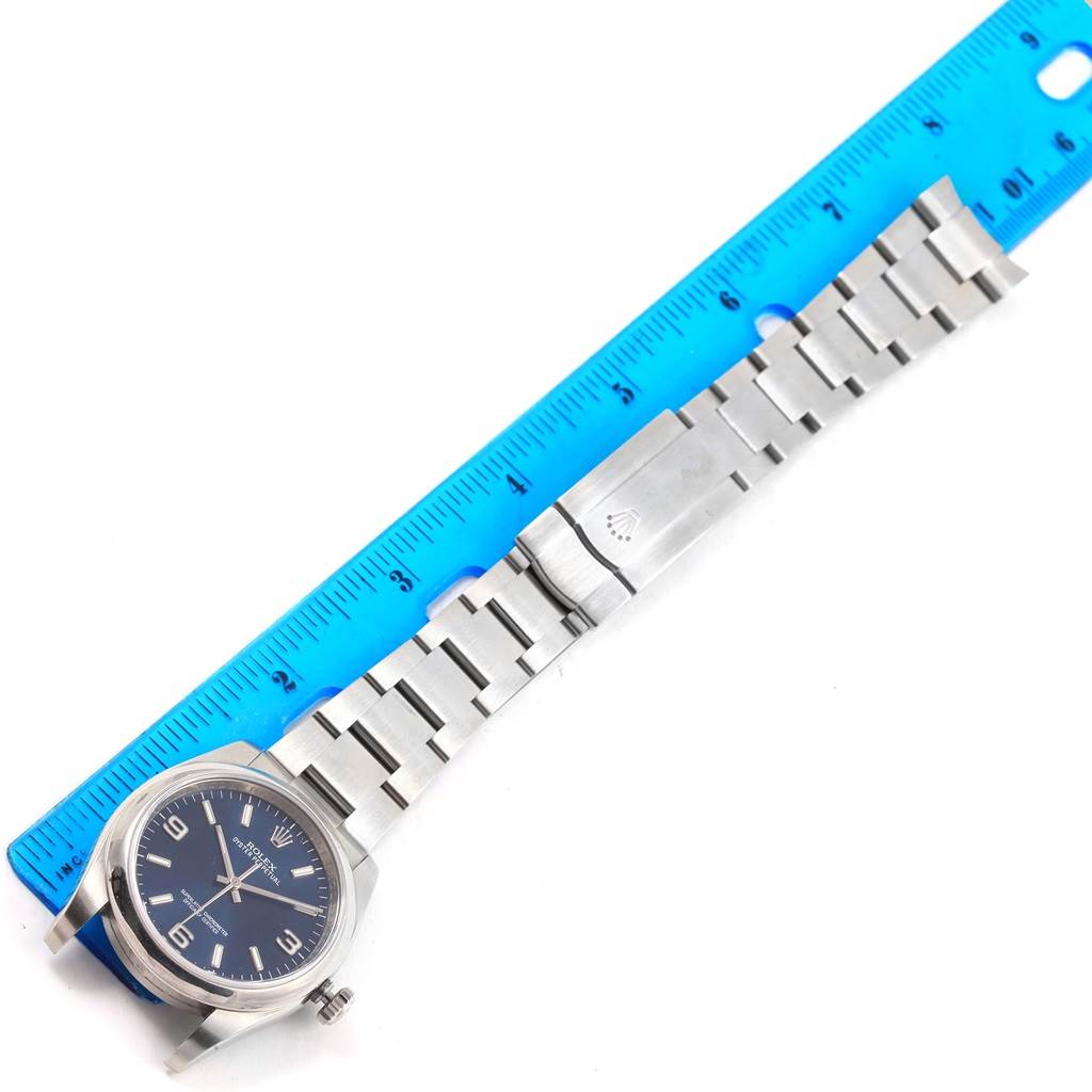 The image shows the Rolex Oyster Perpetual 116000 Men's Stainless Steel Blue Dial 116000 Men's Stainless Steel Blue Dial watch laid flat with its bracelet extended and measured using a blue ruler.