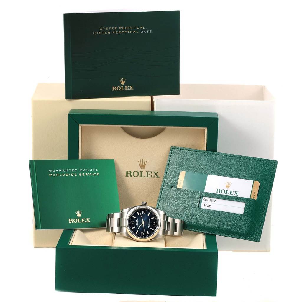 This image shows a Rolex Oyster Perpetual 116000 Men's Stainless Steel Blue Dial 116000 Men's Stainless Steel Blue Dial watch along with manuals, a guarantee card, and the original packaging.